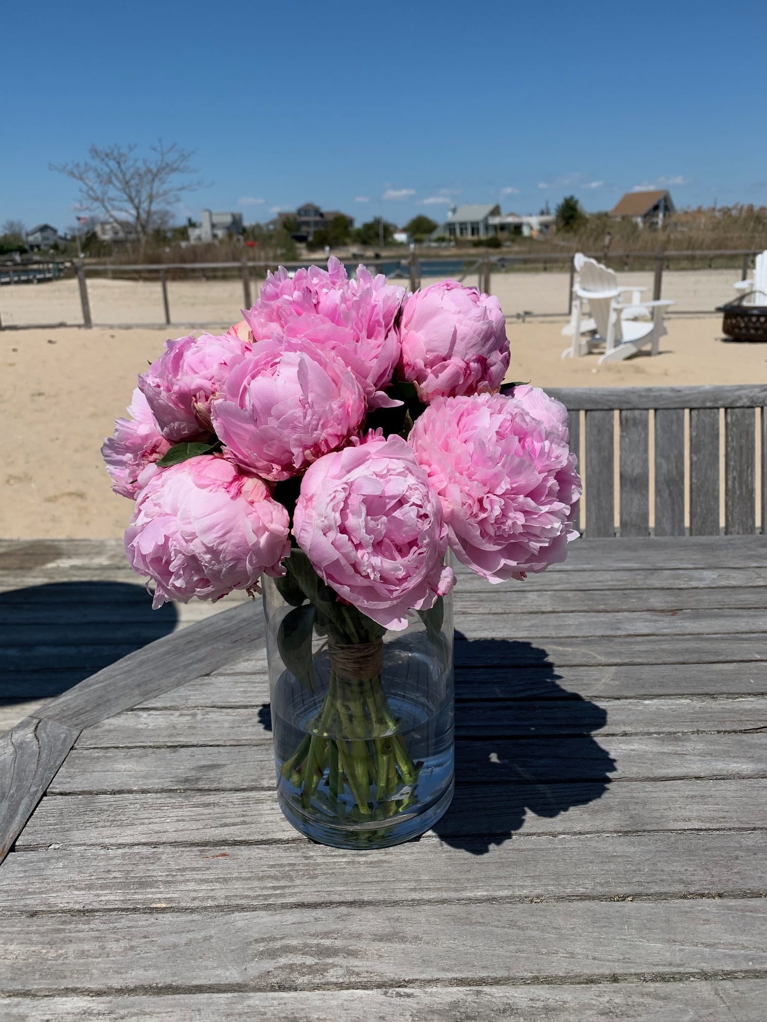 Pink peonies arranged in a clear glass vase on a wooden table.