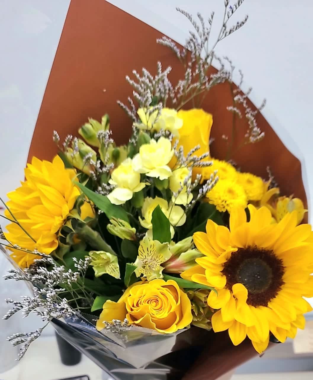 Bouquet of sunflowers, yellow roses, and pale yellow flowers in brown wrap