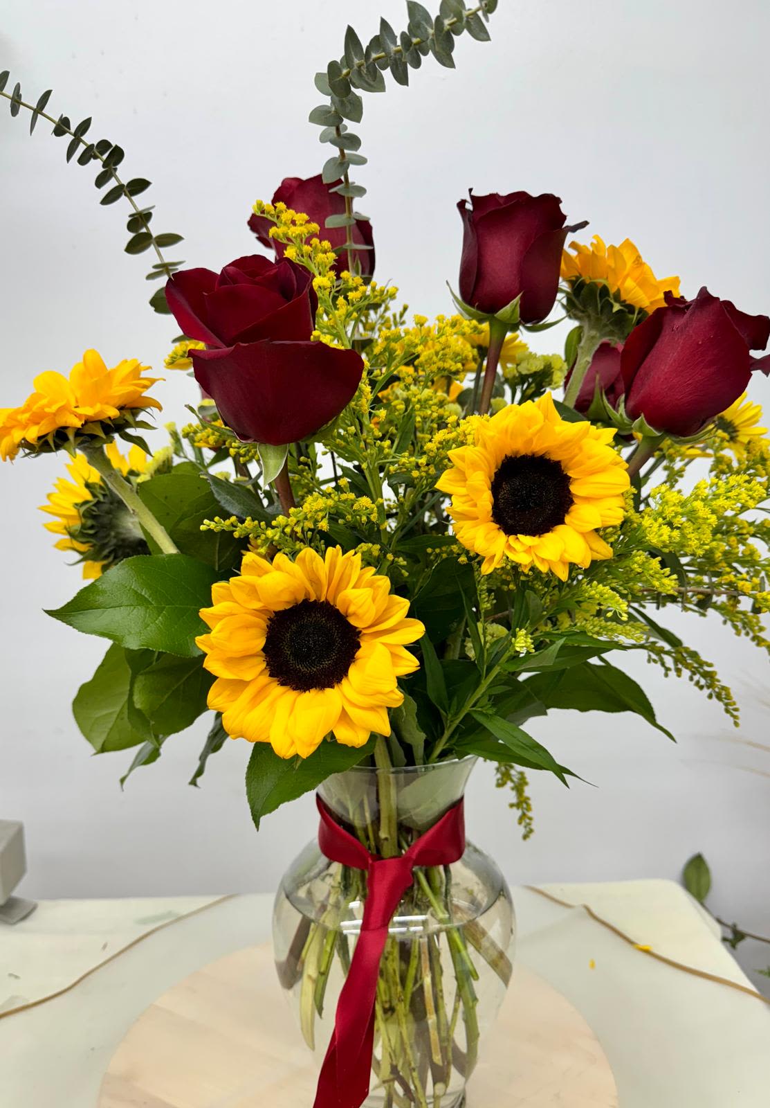 Bouquet of red roses and yellow sunflowers in a glass vase with a red ribbon