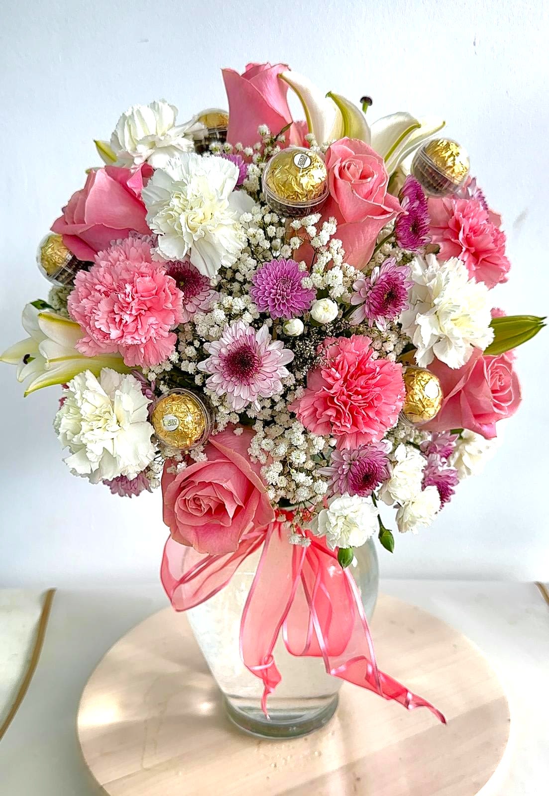Pink and white bouquet in a glass vase with gold chocolates and a pink ribbon