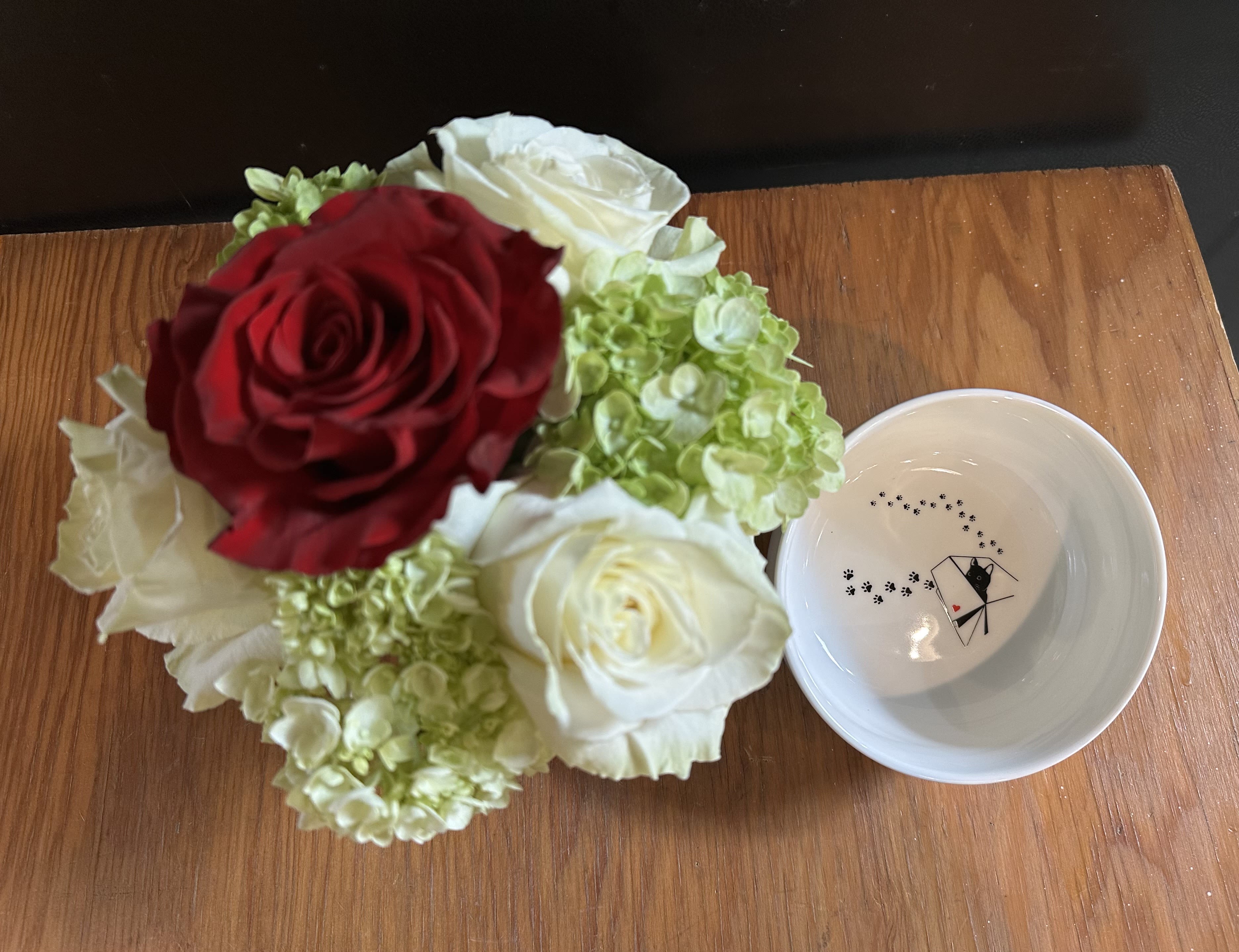 Bouquet of red and white roses with green hydrangeas beside a small white bowl
