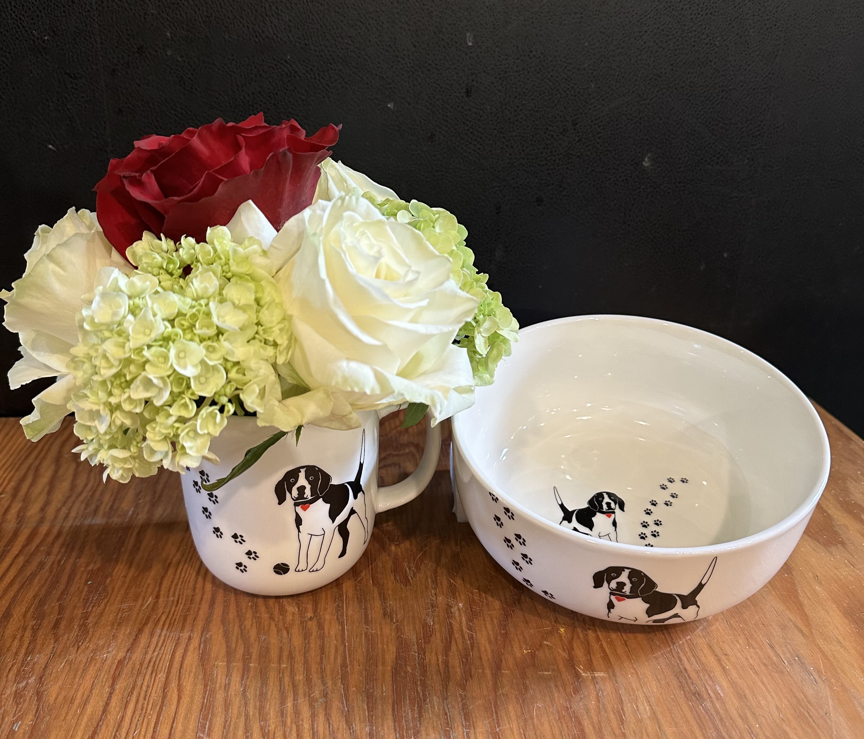 Small bouquet of red, white, and pale green flowers in a dog-print mug beside a matching bowl