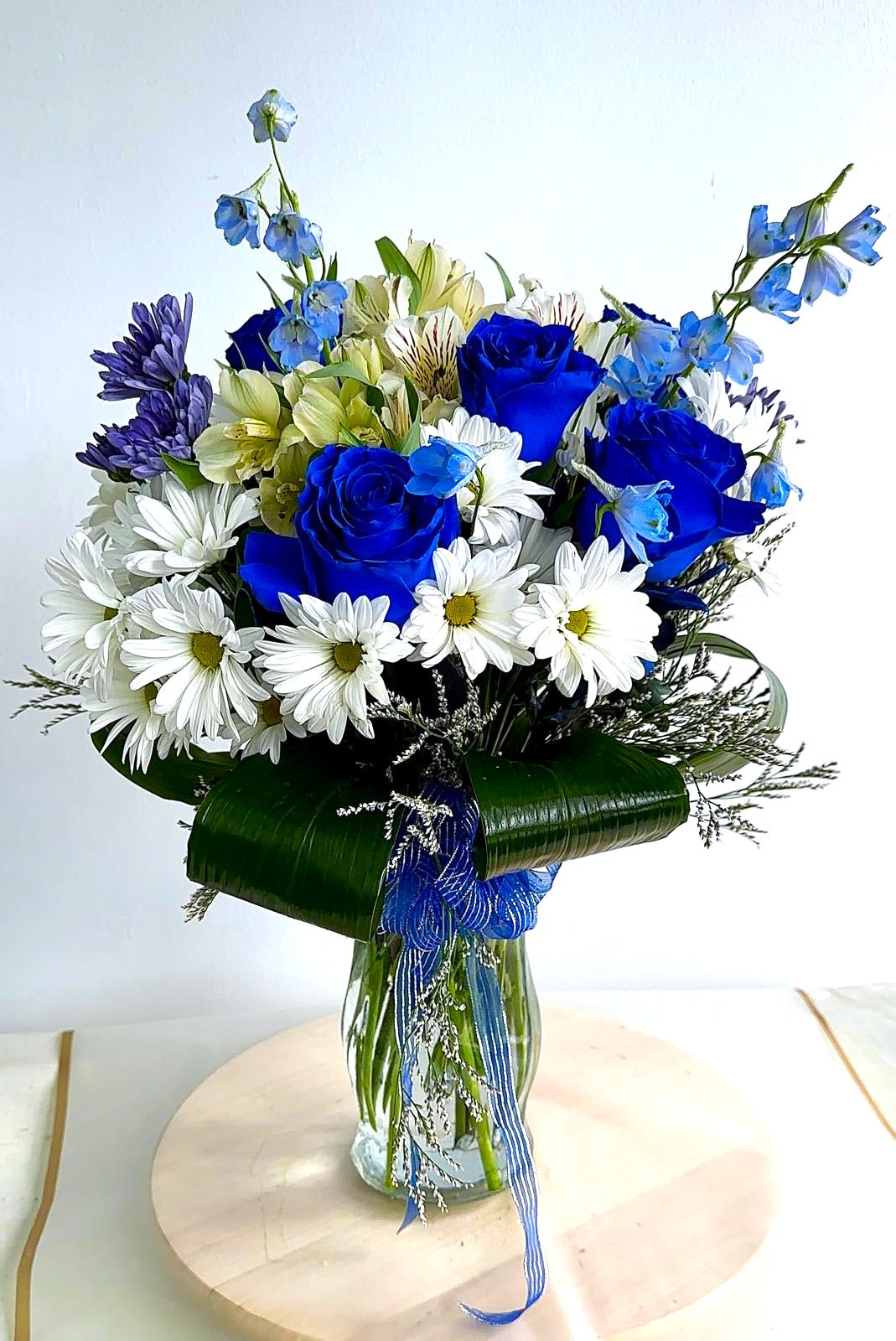 Blue roses and white daisies in a glass vase with ribbon