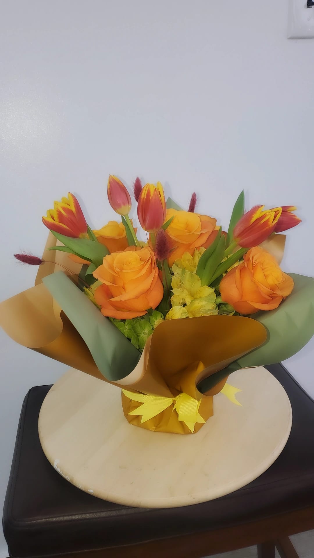 Bouquet of orange roses and red-yellow tulips wrapped in gold and green paper