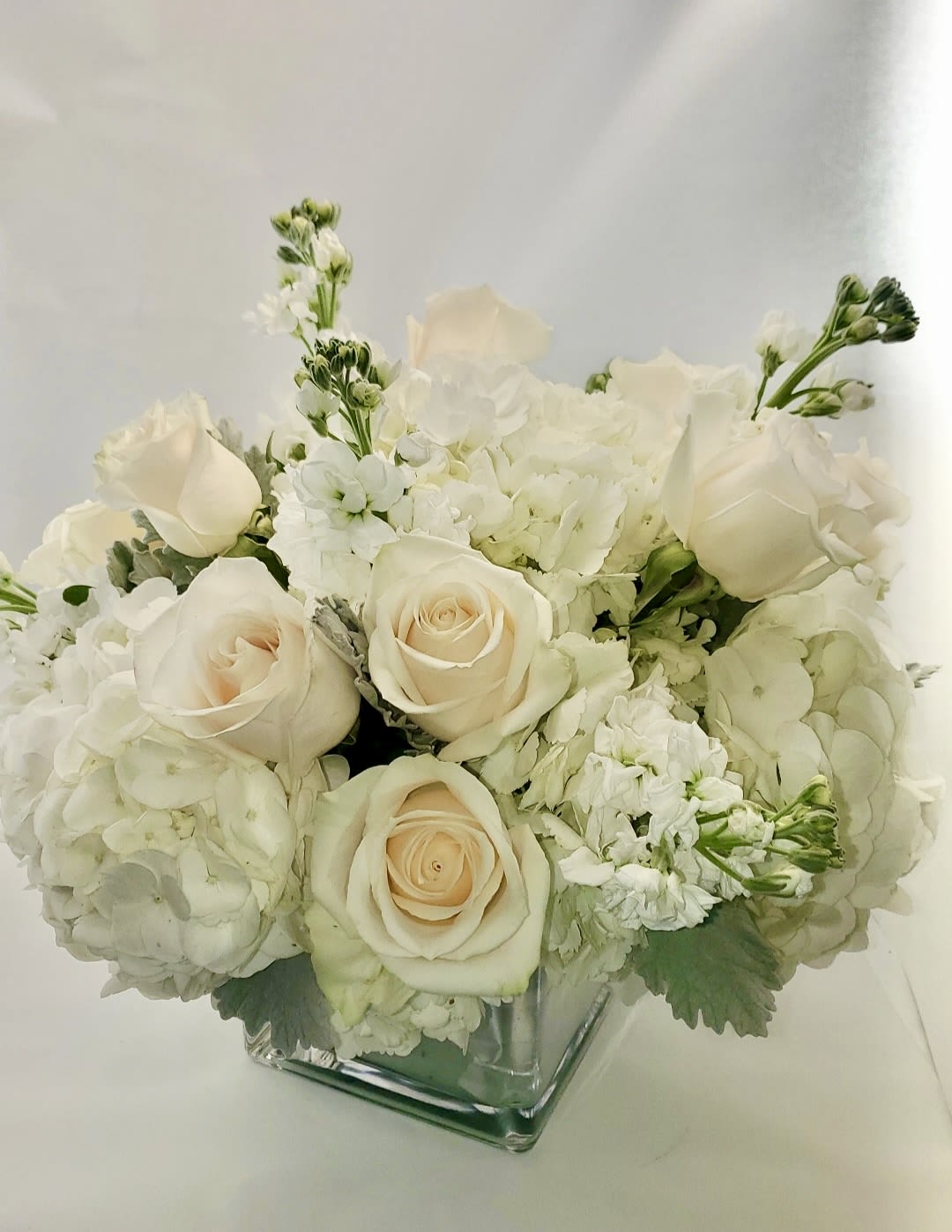White roses and hydrangeas arranged in a square glass vase
