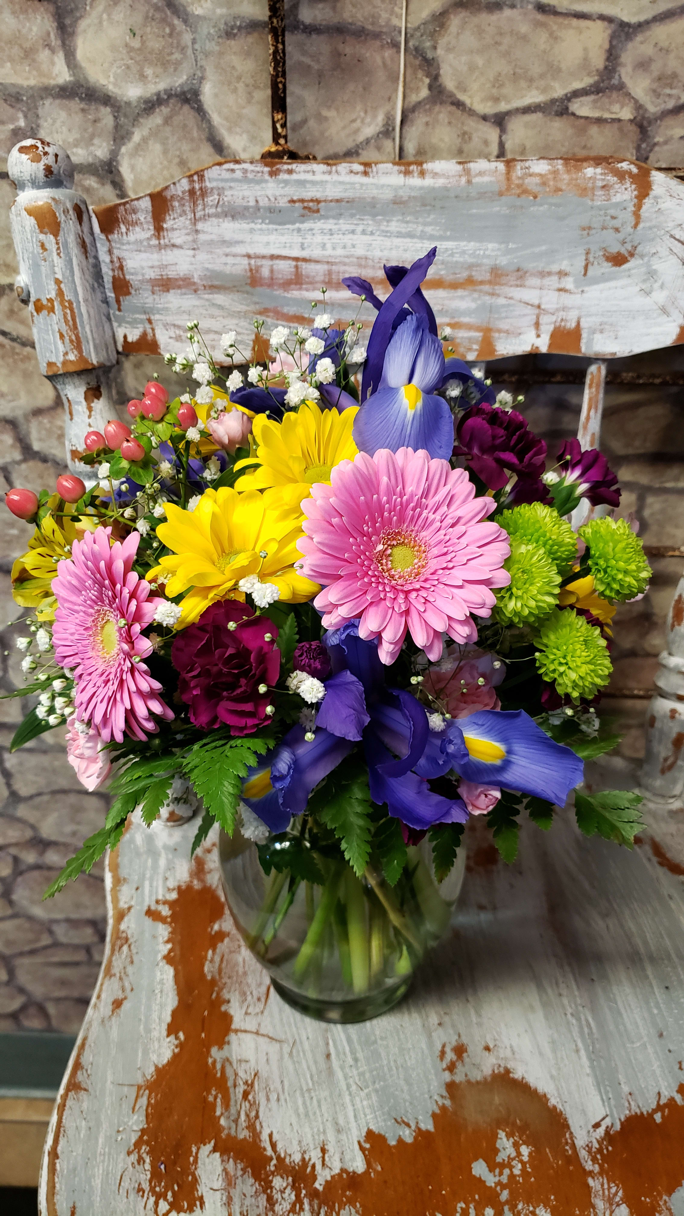 Mixed bouquet of pink, yellow, purple, and blue flowers in a glass vase