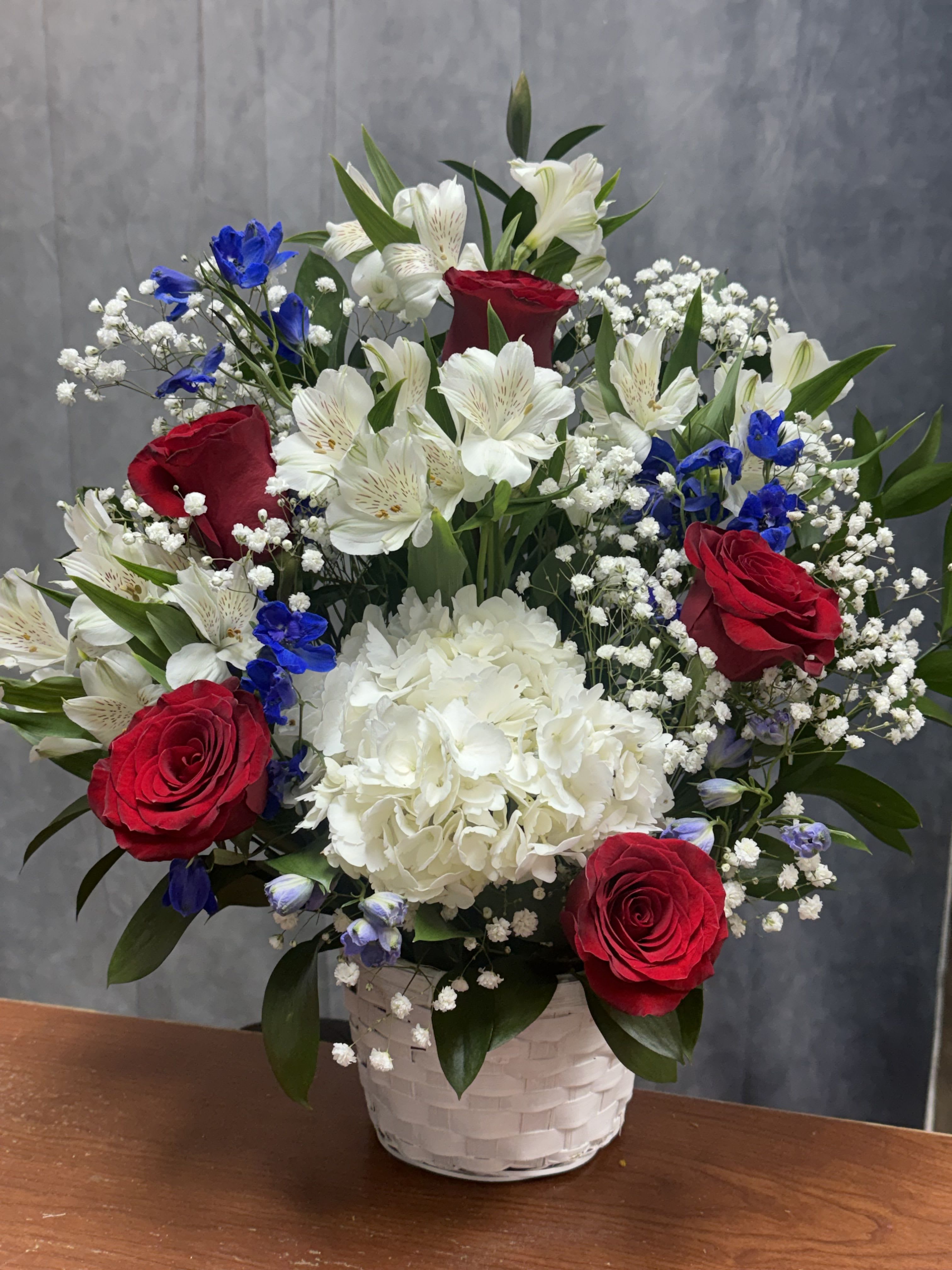 Blue, White and Red Basket - Red roses, white hydrangeas and lilies with blue accents in a white woven basket-lush, layered and classic; perfect for any occasion or patriotic celebrations.