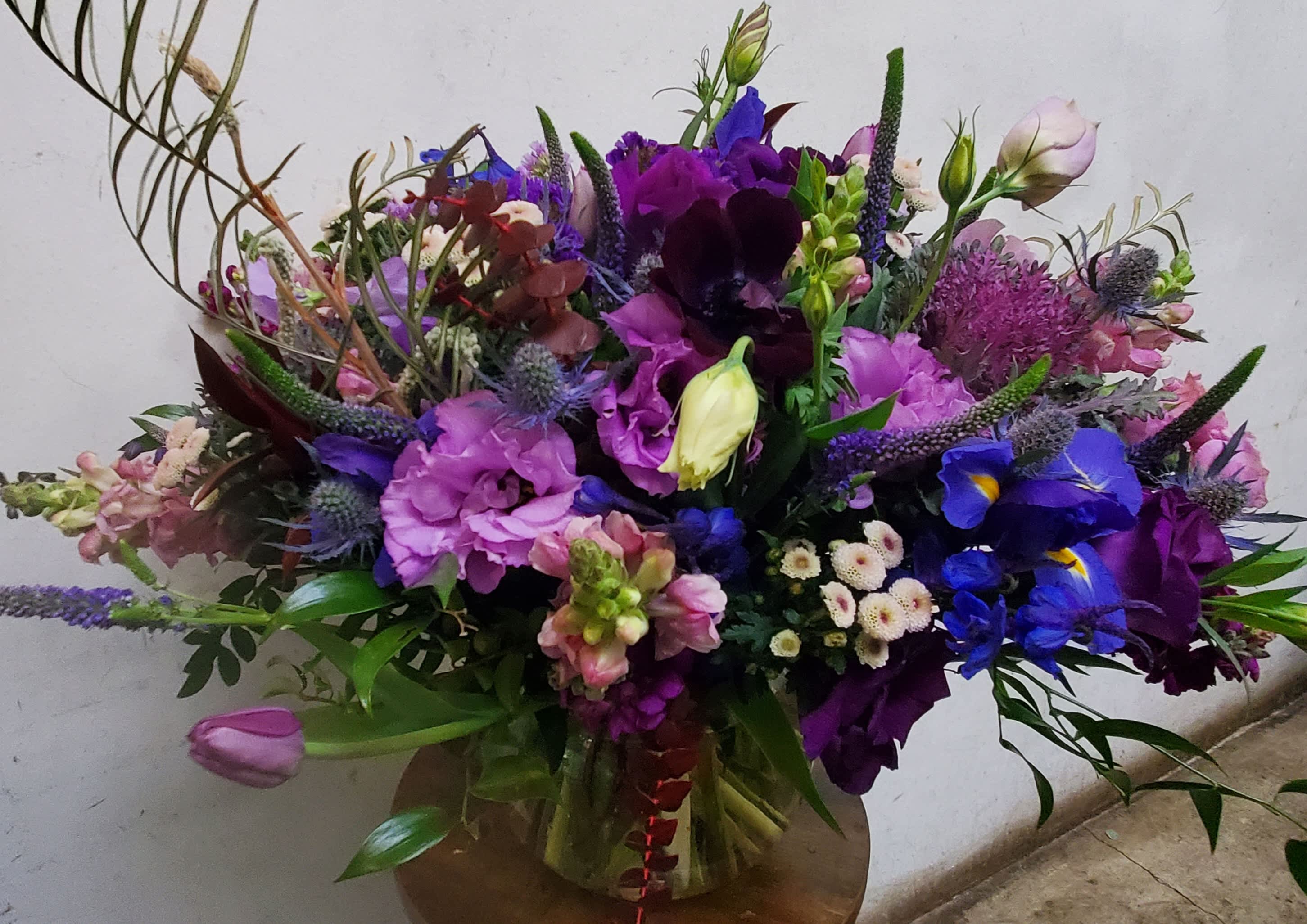 Large mixed bouquet of purple, pink, and blue flowers in a glass vase