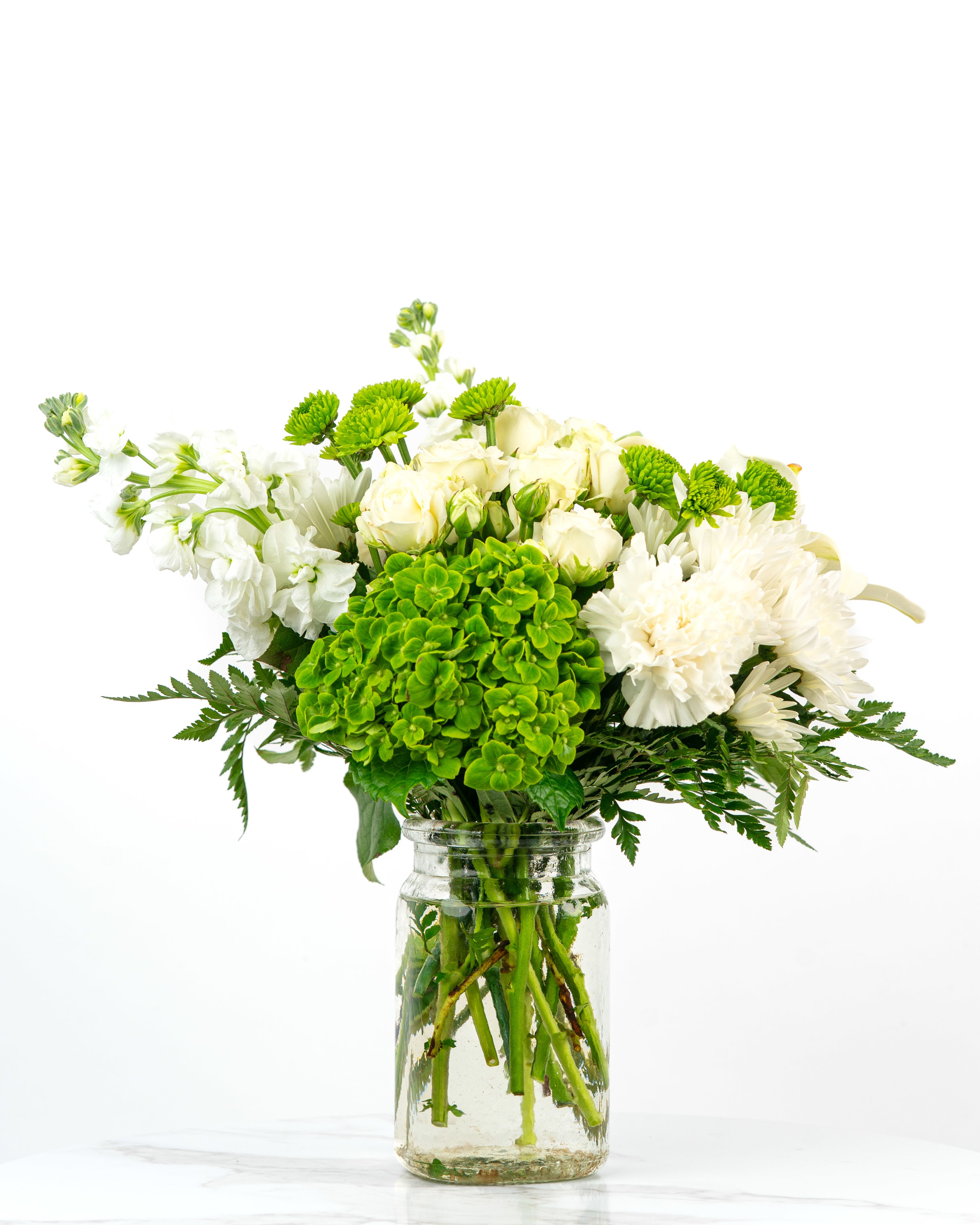 White and green mixed flower arrangement in a clear glass jar vase