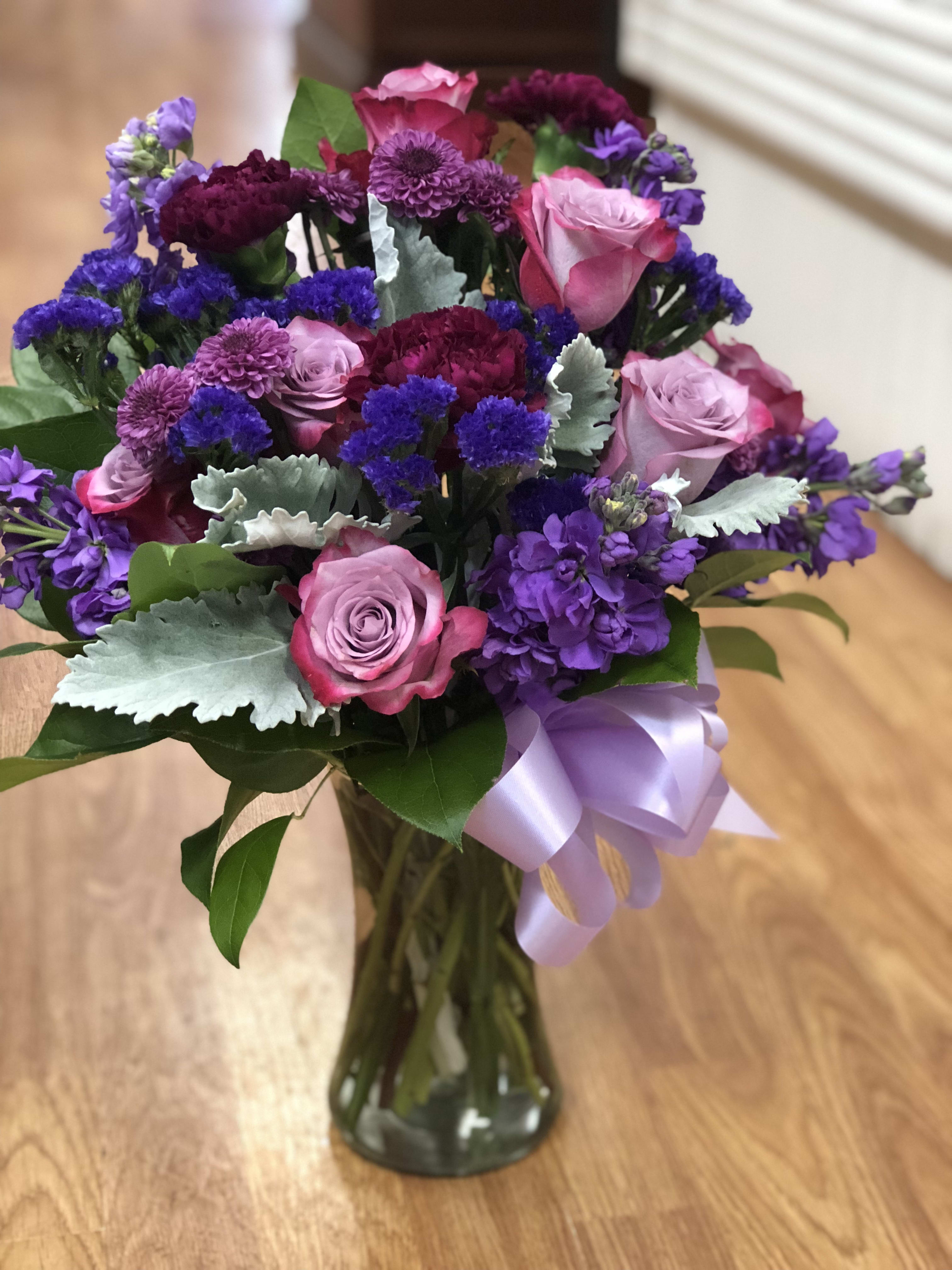 Bouquet of pink and purple flowers in a glass vase with a lavender ribbon