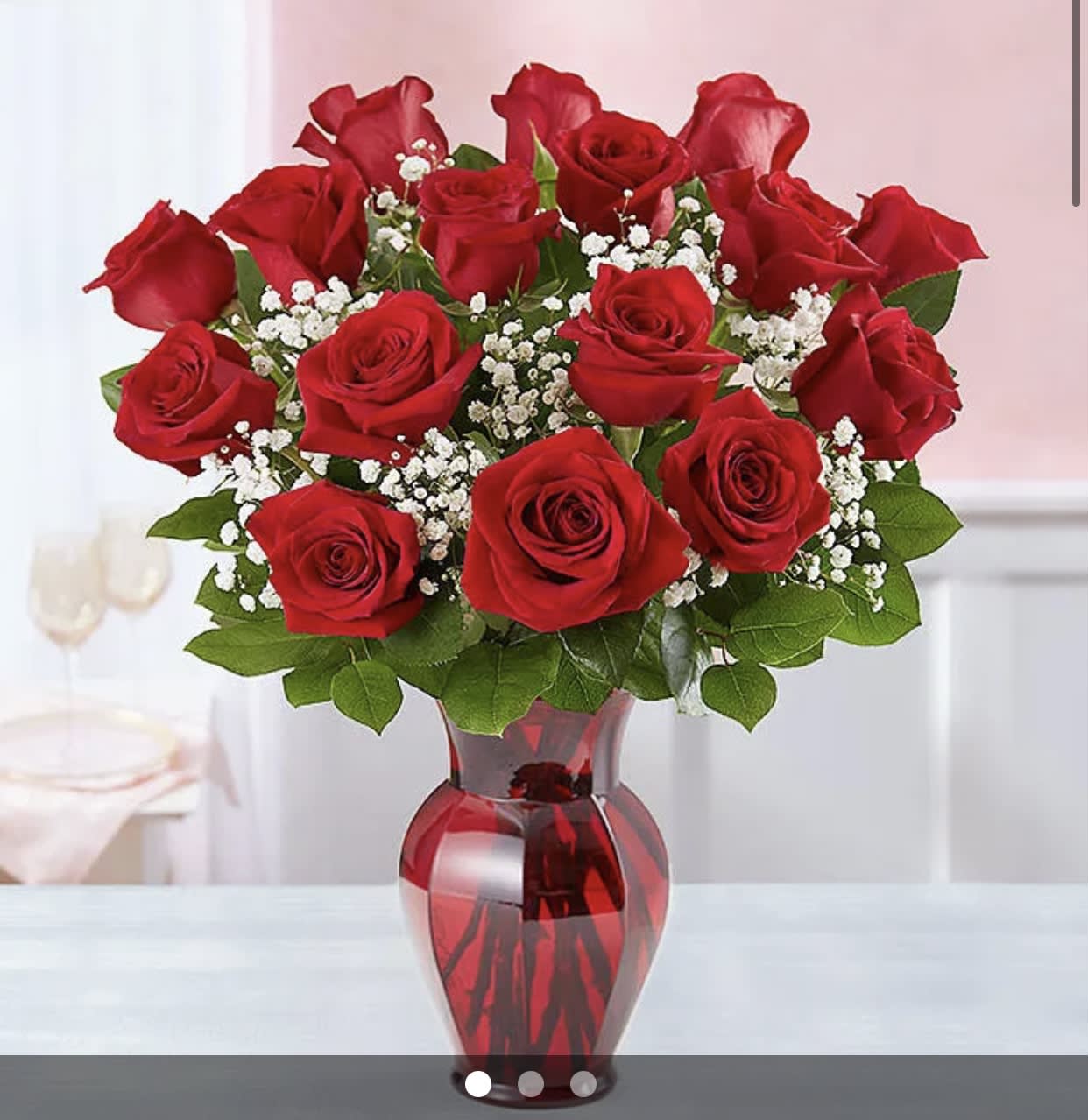 Red roses arranged in a red glass vase with white filler flowers