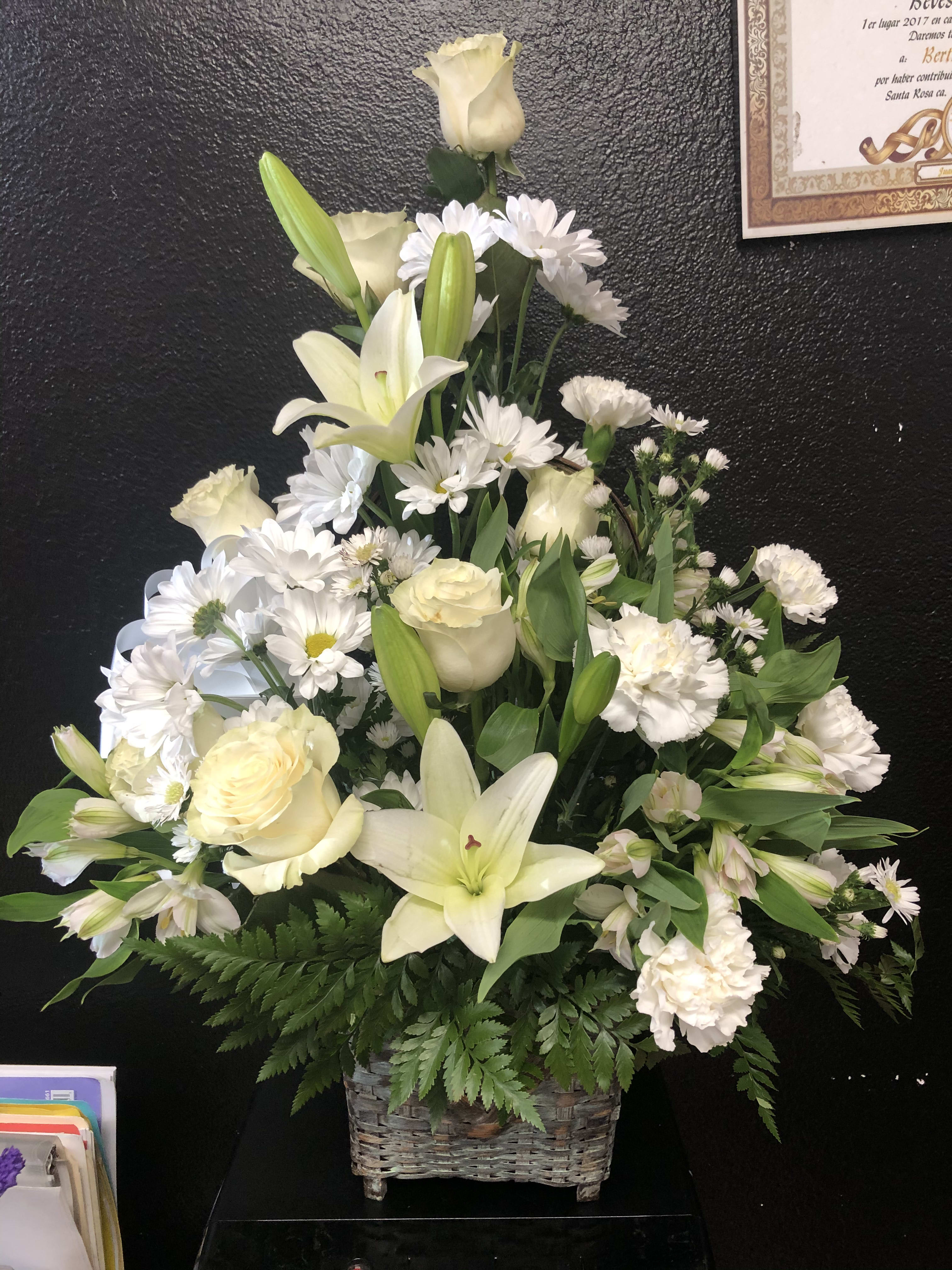 White lilies and roses arranged in a wicker basket with white daisies