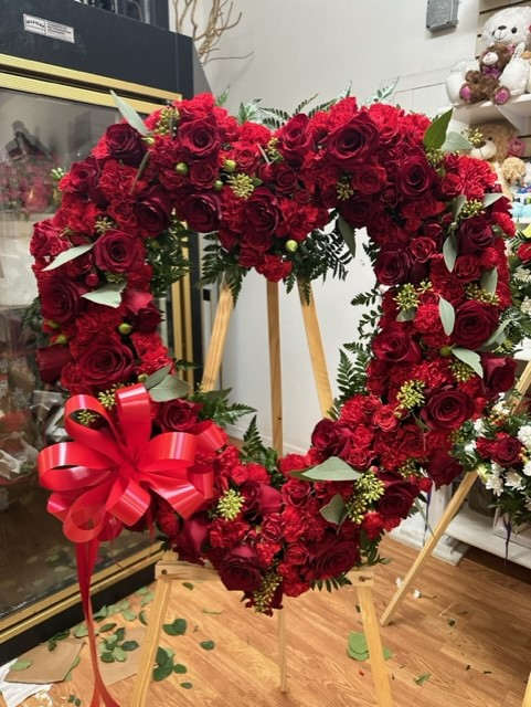 Heart-shaped red rose wreath on a wooden stand with a red ribbon
