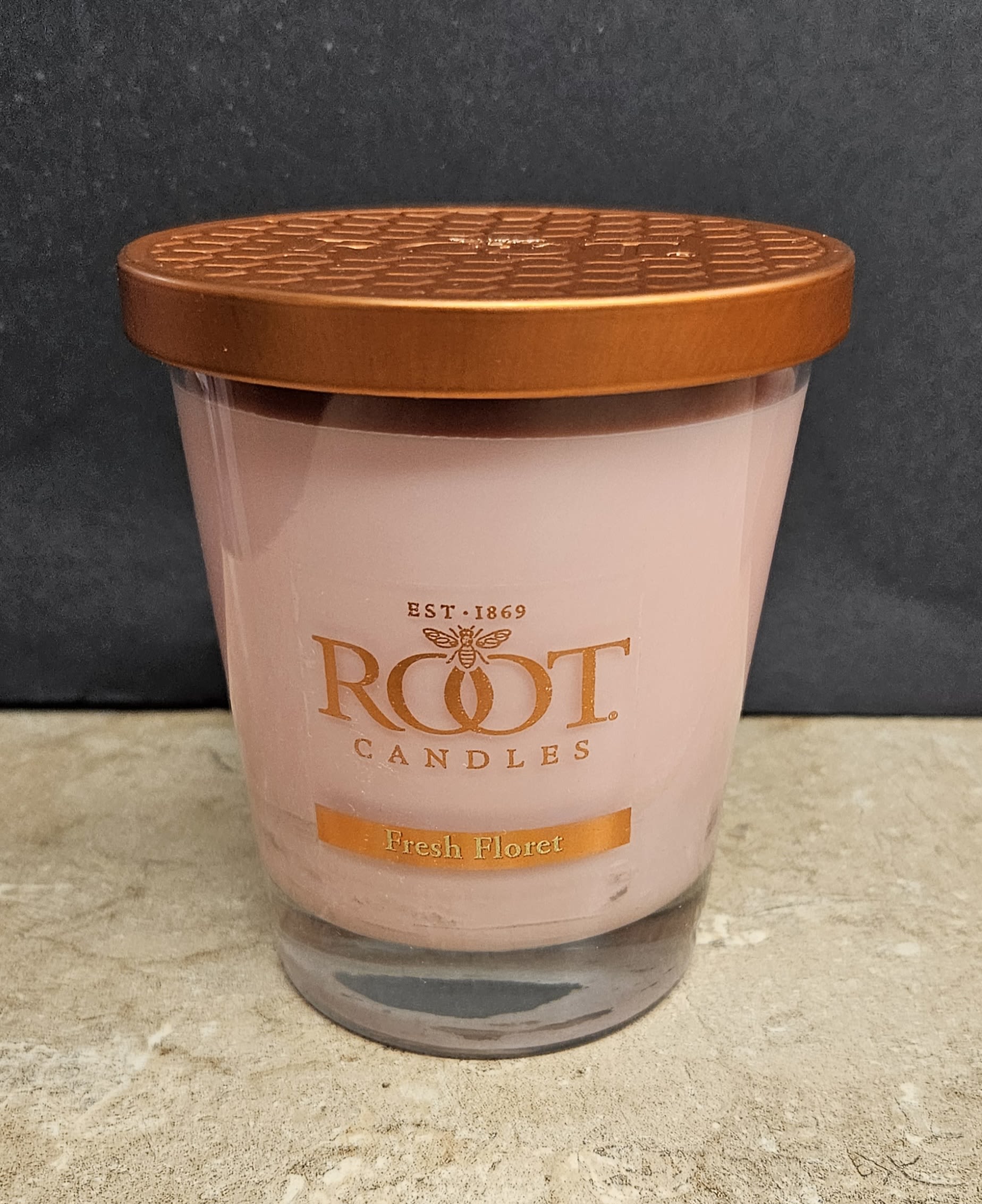 Root Candle Fresh Florist M - A soft blush Root Candle in a clear glass jar creates an immediate sense of calm-perfect as a small gift or thoughtful add-on for birthdays, housewarmings, or "just because" moments. This scented candle reads like a simple, polished present that will make the person you're thinking of feel cozy and cared for without fuss.  The single candle comes in a clear glass jar topped with a copper-toned metal lid and pale pink wax labeled Root Candles with the scent name Fresh Floret. The warm neutral palette and clean design suit most décor styles; it pairs beautifully with fresh pink or orange blooms as a table accent or bedside treat. Small and ready to gift, it's an everyday, giftable choice that brings a lingering floral aroma and a calm, homey presence to any room.