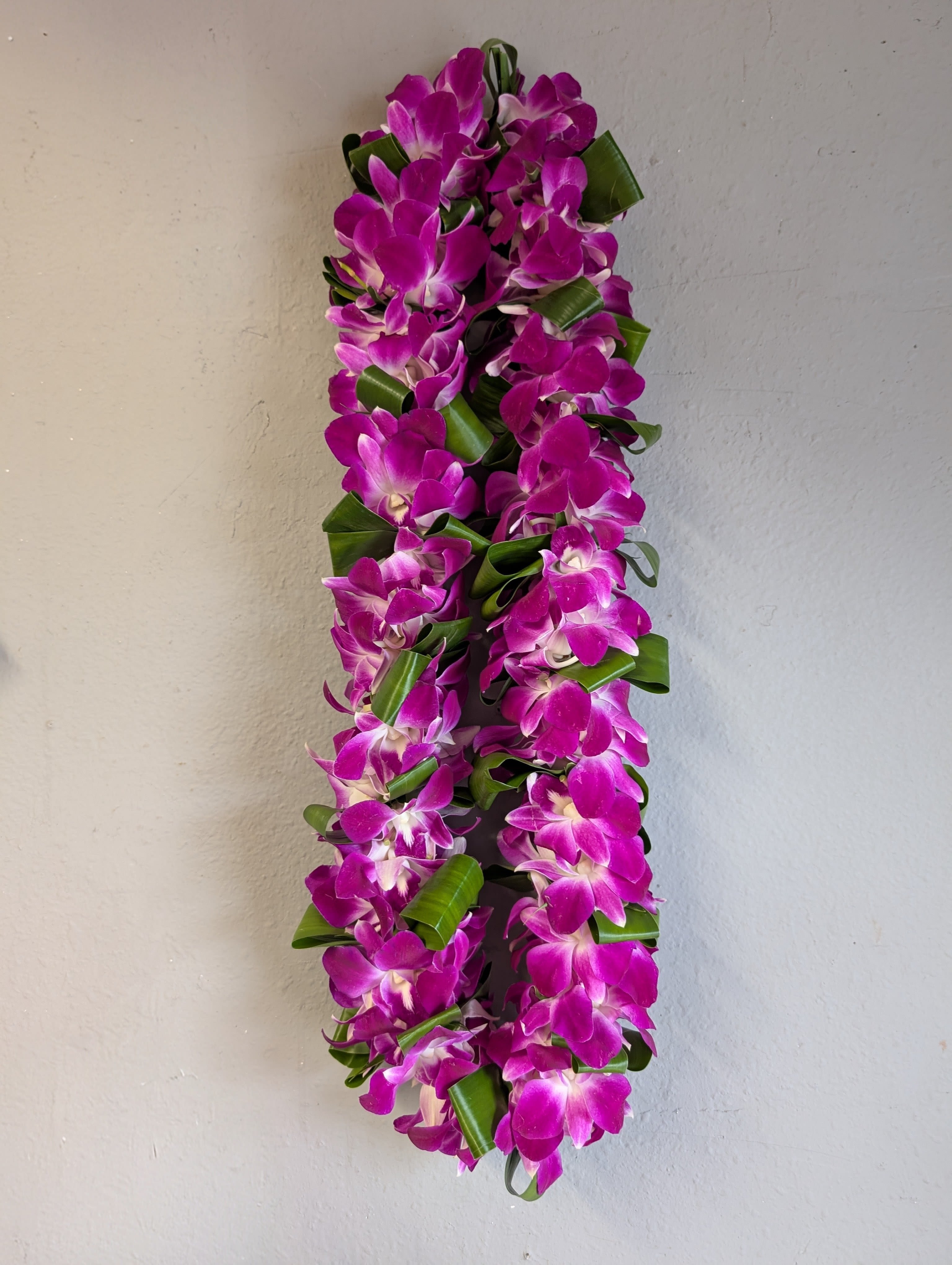 Bombay and Ti leaves lei - double.  - A lush double lei of densely strung purple orchids with white centers, accented by folded green ti-style leaves - a vibrant choice for a graduation Lei. 