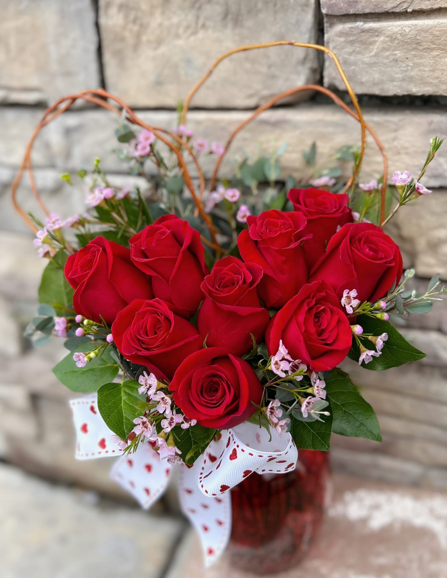Red roses arranged in a glass vase with a heart-patterned ribbon