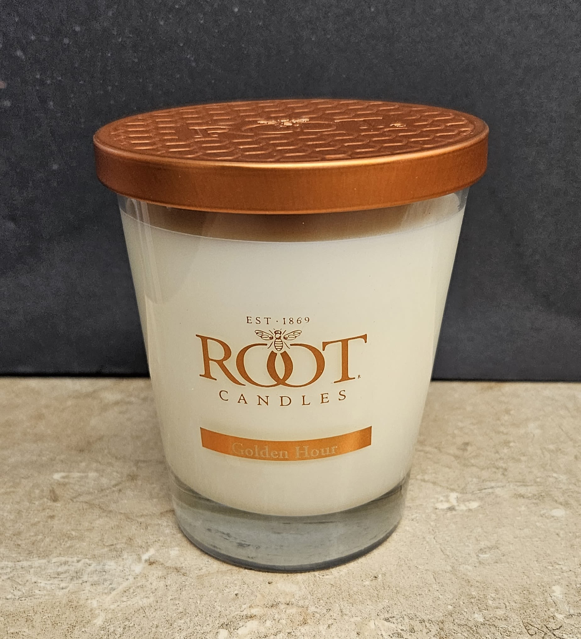 Root Candle Golden Hour M - Warm, amber-glow fragrance meets simple, modern design in this Root Candle Golden Hour M-an ideal housewarming or hostess gift that brings a cozy, sunset-like scent to any room. As a scented candle for gifting, it announces care and calm: the person you're thinking of will notice the gentle golden notes and appreciate the clean, retail-ready presentation.  The candle comes in a clear glass tumbler with smooth white wax and a copper-toned metal lid, labeled "Root Candles" with the scent name Golden Hour for easy identification. Compact and versatile, the medium size fits on a bedside table, bathroom shelf, or living room mantel and pairs beautifully with white, orange, or neutral décor. The included metal lid keeps the scent fresh between uses; simply trim the wick and keep the glass on a heat-safe surface when burning.