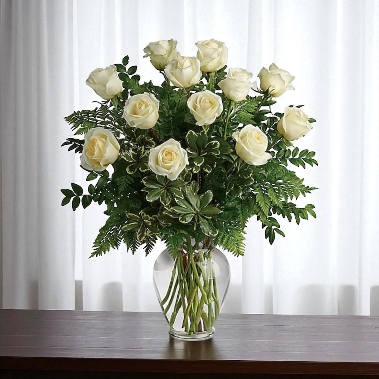 White roses arranged in a clear glass vase with greenery