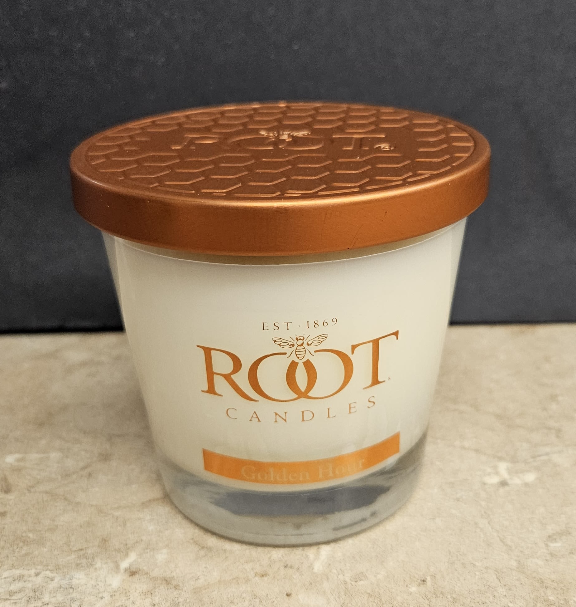 Root Candle Golden Hour S - Golden Hour brings a warm, cozy glow to any room - a perfect small gift for Father's Day, a housewarming, or a thoughtful Just Because moment. This flower arrangement listing pairs that mellow amber feel with clean white and orange accents to complement seasonal displays for Memorial Day, Autumn gatherings, or cozy winter nights; the presentation reads like a curated gift set meant to make the person you're thinking of feel comforted and seen.  The centerpiece is a single Root candle in a clear glass jar topped with a copper-colored metal lid, featuring smooth white wax and an orange-accented label for a simple, homey look. Though framed here among floral offerings, the clean lines and warm hues make it easy to tuck into a larger bouquet or give on its own alongside seasonal blooms for Thanksgiving, Christmas, birthdays, anniversaries, or sympathy and funeral arrangements.  Ideal for bedside tables, mantels, or a kitchen counter, this compact candle complements gifts for graduation, retirement, new baby celebrations, and more - or as a gentle Get Well or Thinking of You gesture. Burn responsibly: trim the wick to 1/4" before lighting and keep away from drafts and flammable materials; available in size S to fit small gift boxes or floral bundles.