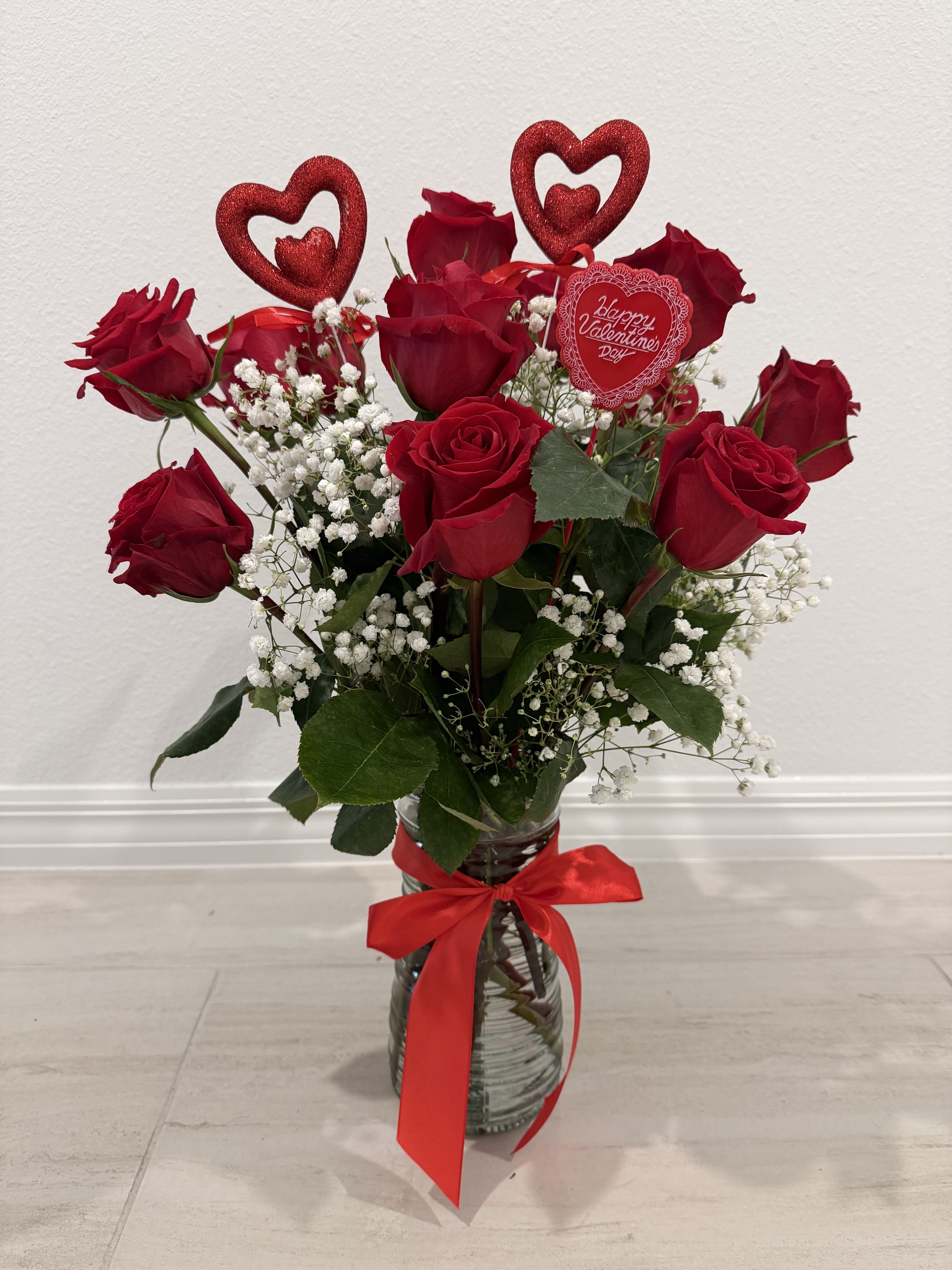 Red roses in a glass vase with baby's breath and a red ribbon