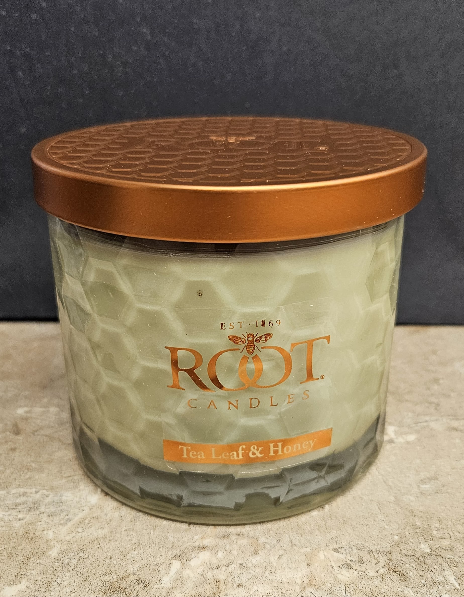 Root Candle Tea leaf &amp; Honey L - Warm, cozy, and quietly elegant-this Root Candle Tea Leaf &amp; Honey jar candle makes a thoughtful housewarming gift or a small everyday present for someone who appreciates soothing home fragrances. As a home décor and gift item, it suits occasions like a birthday, thank-you, or just-because moment when you want the person you're thinking of to feel comforted and cared for.  The candle sits in a clear, faceted glass jar with pale wax and a warm orange label, topped by a copper-toned metal lid that adds a touch of polish to mantel, bedside table, or kitchen shelf. Colors read orange, white, and black in the design, giving a warm, modern look that complements a range of interiors. Lightweight and easy to display, it's the kind of candle that brings a calm, domestic atmosphere to a room-pair it with a handwritten note for an extra personal touch.