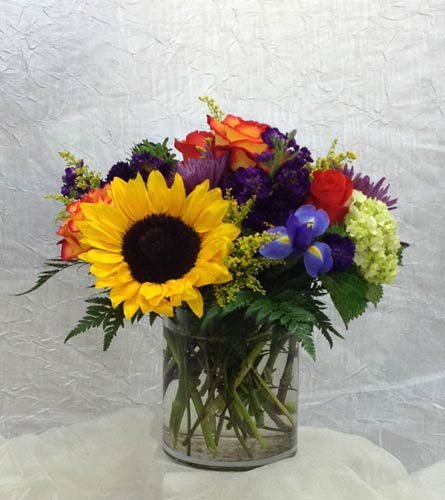 Mixed bouquet with a sunflower, roses, and purple flowers in a glass vase