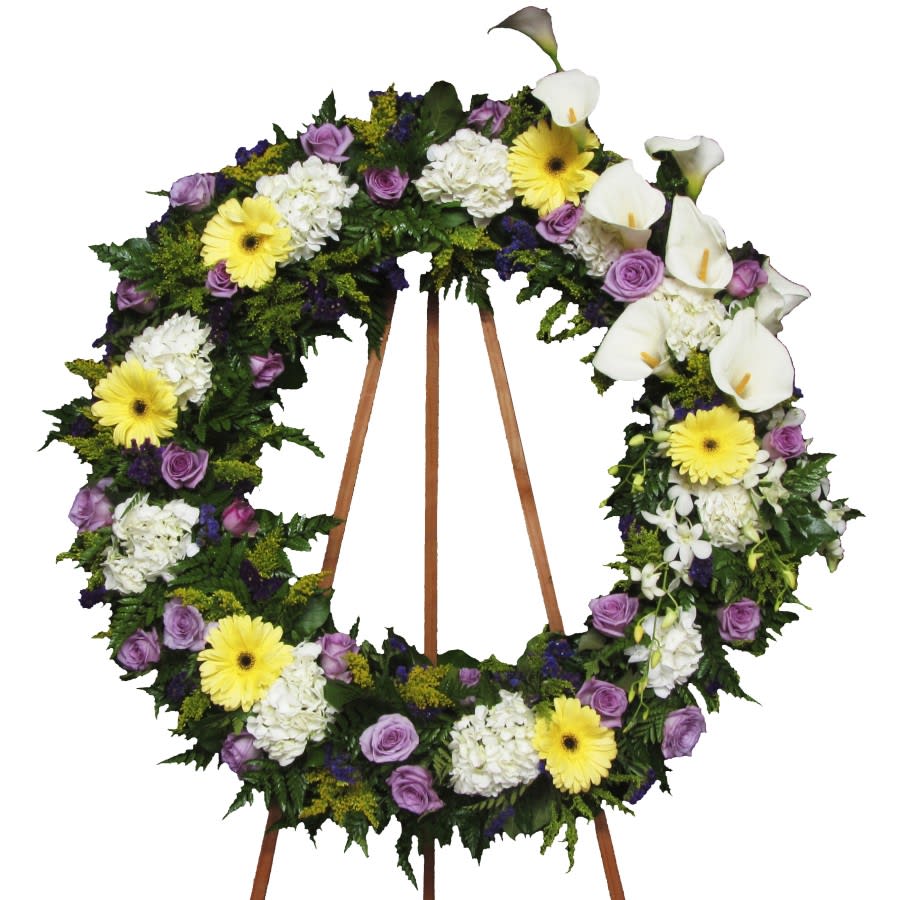 Large floral wreath with white calla lilies, yellow daisies, and purple roses on a stand
