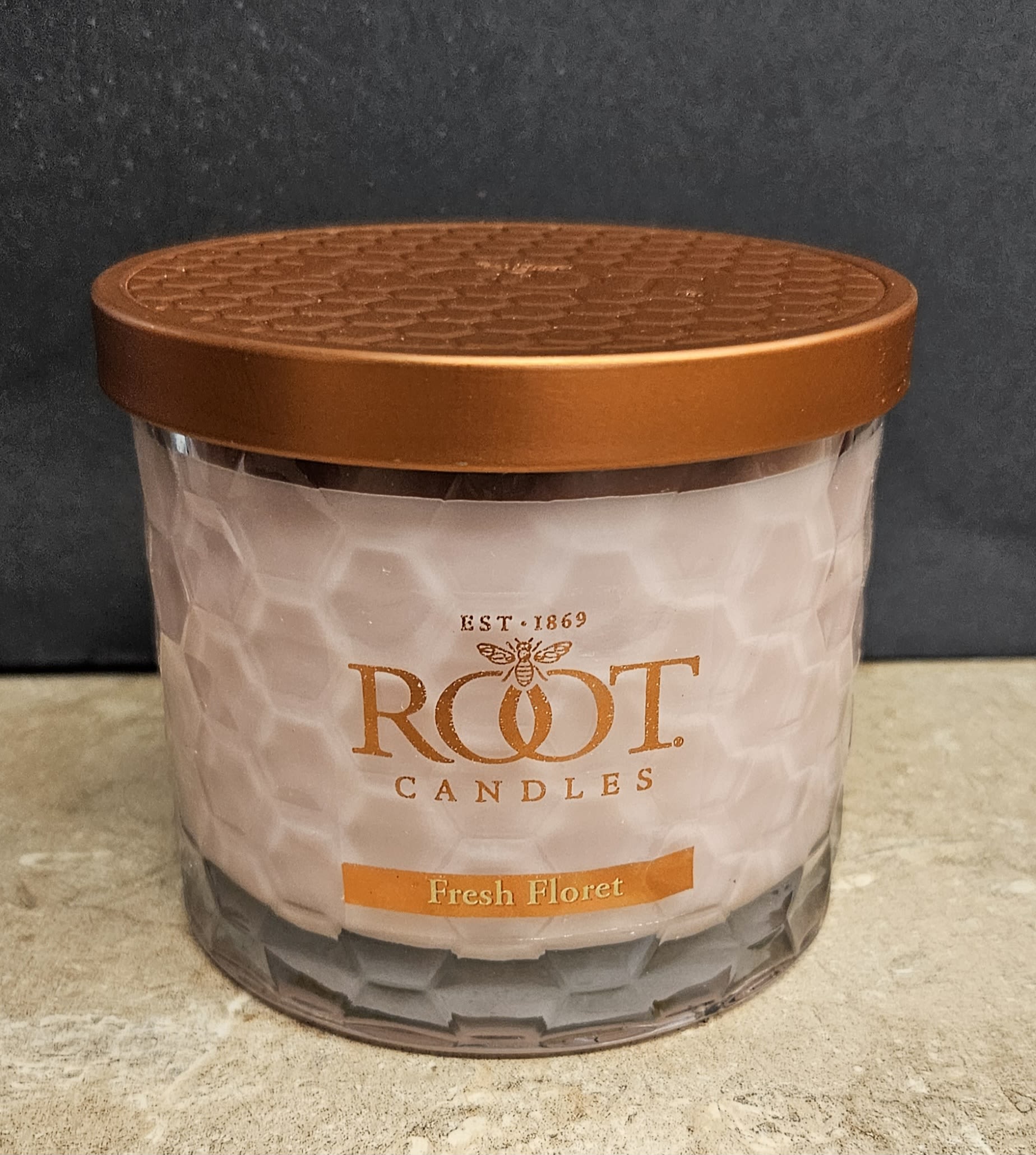 Root Candle Fresh Floret M - Warm, cozy scent meets clean design in this Root Candle Fresh Floret jar-an elegant gift for birthdays, housewarmings, or as a thoughtful "thinking of you" present. The candle arrives in a clear faceted glass container with a copper-colored metal lid and a simple label that reads Root Candles Fresh Floret; the soft white wax suggests a fresh, floral-fruity fragrance that helps a recipient feel welcomed and comforted.  This medium-size candle (jar style with metal lid) pairs beautifully with contemporary home decor-white wax, clear glass facets, and warm copper accents create a subtle, polished look that works on mantels, kitchen counters, or bedside tables. Packaged as a giftable fragrance item rather than a bouquet, it's an ideal choice when you want to send a lasting, scent-driven reminder: perfect for friends settling into a new place, someone needing a little uplift, or anyone who appreciates understated, modern home accessories.