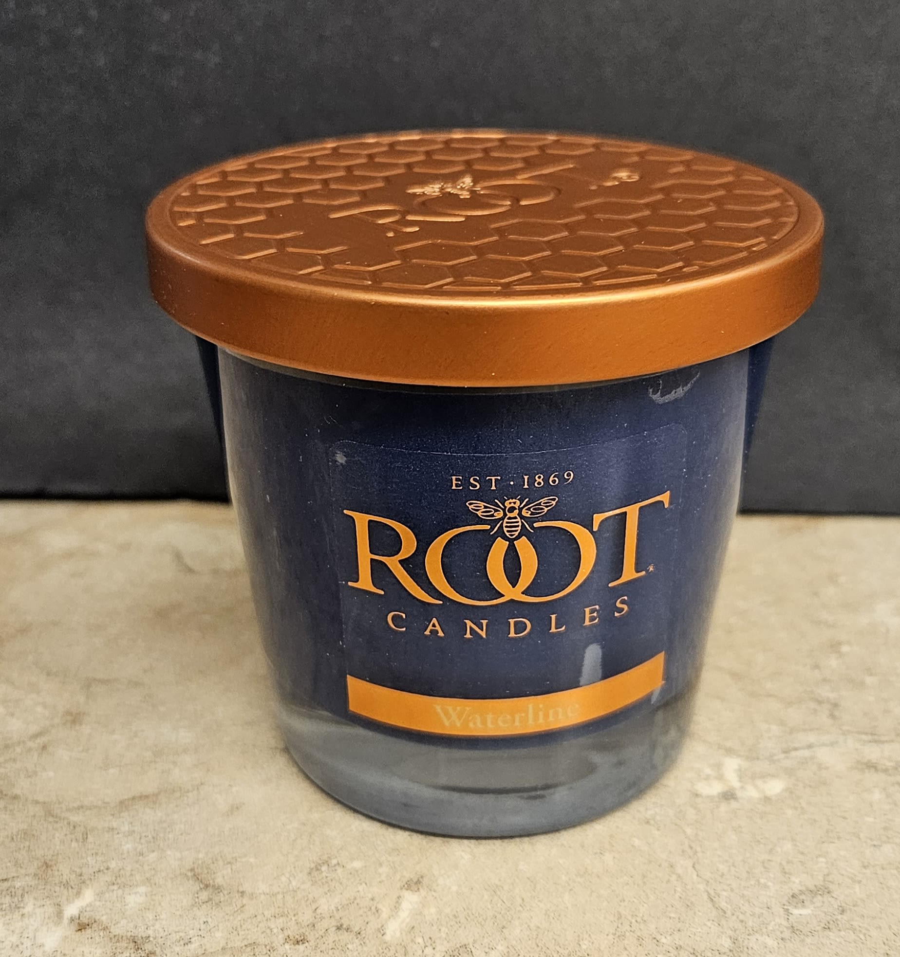Root Candle Waterline M - Moody deep blue glass and a metallic orange lid give this Root Candle Waterline S a striking, contemporary look - perfect as a thoughtful gift or a subtle home accent. As a scented candle for everyday gifting, it works beautifully for housewarming, hostess gifts, birthdays, or just to let someone know you're thinking of them; the recipient will enjoy a calm, upscale presence on a coffee table or bedside tray.  This single scented candle comes in a dark blue glass jar labeled "Root Candles" with the fragrance noted as Waterlily. The compact size makes it easy to place in small spaces, and the included metal lid keeps fragrance fresh between uses. The blue, orange, and black color palette creates a sophisticated contrast that complements modern decor without overwhelming it.  Ideal for someone who appreciates refined, contemporary home fragrances, this candle offers an elegant way to add a soft floral-woody scent to living rooms, bathrooms, or entryways. For best results, place on a heat-resistant surface, trim the wick to 1/4" before each burn, and keep away from drafts to ensure an even melt pool and longer-lasting scent.