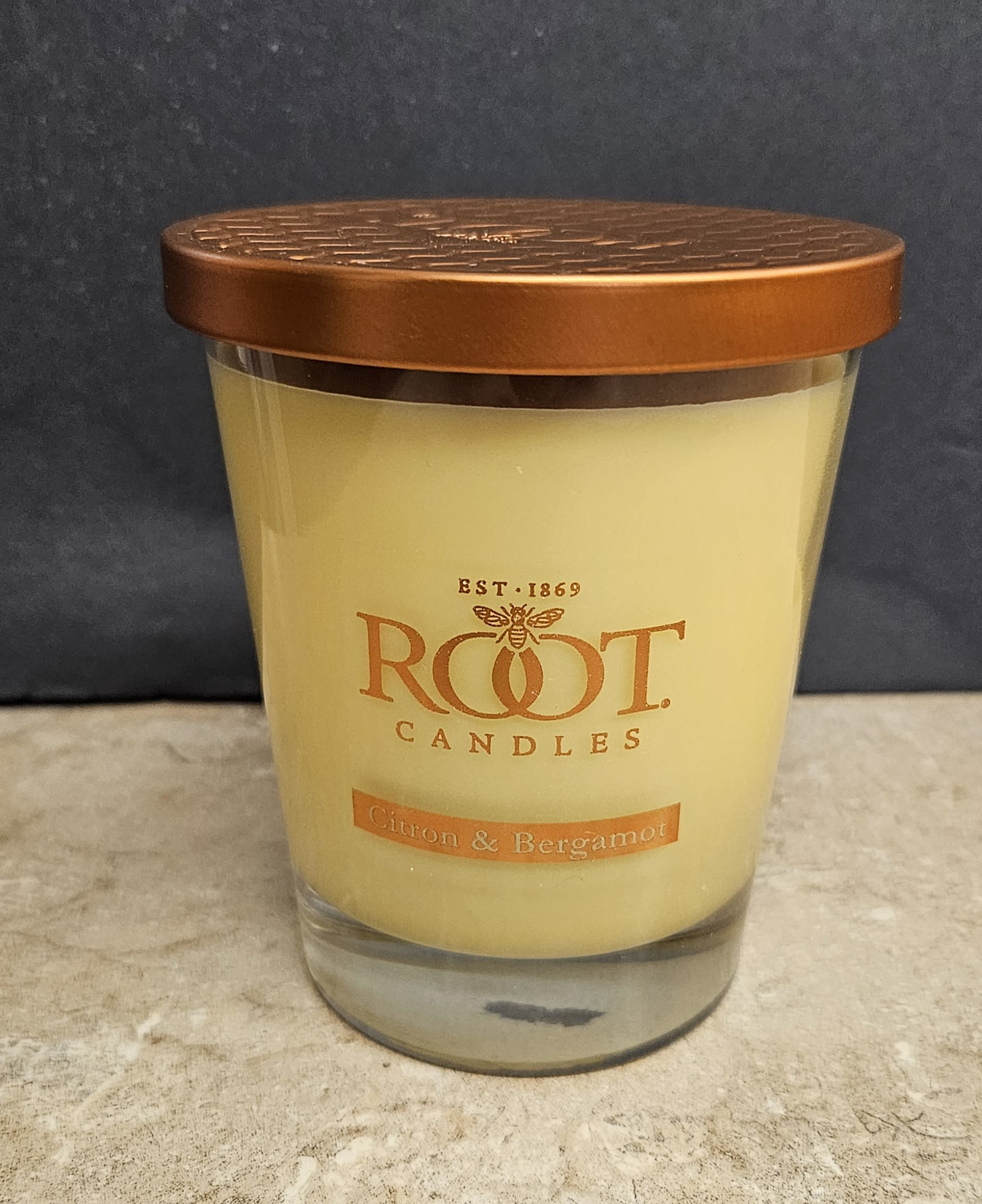 Root Candle Citron &amp; Bergamot L - Bright, uplifting citrus notes make this housewarming gift feel like sunshine in a room - a citron &amp; bergamot scented candle perfect for everyday cozy moments and thoughtful housewarmings. This flower-arrangement page presents the candle as a companion gift for birthday bouquets or thank-you deliveries, adding a warm glow and fresh, zesty scent that helps the person you're thinking of settle in and smile.  The candle arrives in a clear glass jar topped with a copper-colored metal lid; the pale yellow wax and simple Root Candles label give it a clean, modern look that complements yellow and orange floral palettes. Sized as a medium (M), it fits neatly on mantels, kitchen counters, or bedside tables and pairs beautifully with sunflowers, orange roses, or mixed seasonal stems for a coordinated gift.  Choose this scented candle to round out a bouquet for a new home, hostess gift, or "thinking of you" delivery - the kind of extra that makes someone feel noticed. Standard care: keep wick trimmed to 1/4" and place on a heat-safe surface; burn within sight and away from drafts for best fragrance and safety.
