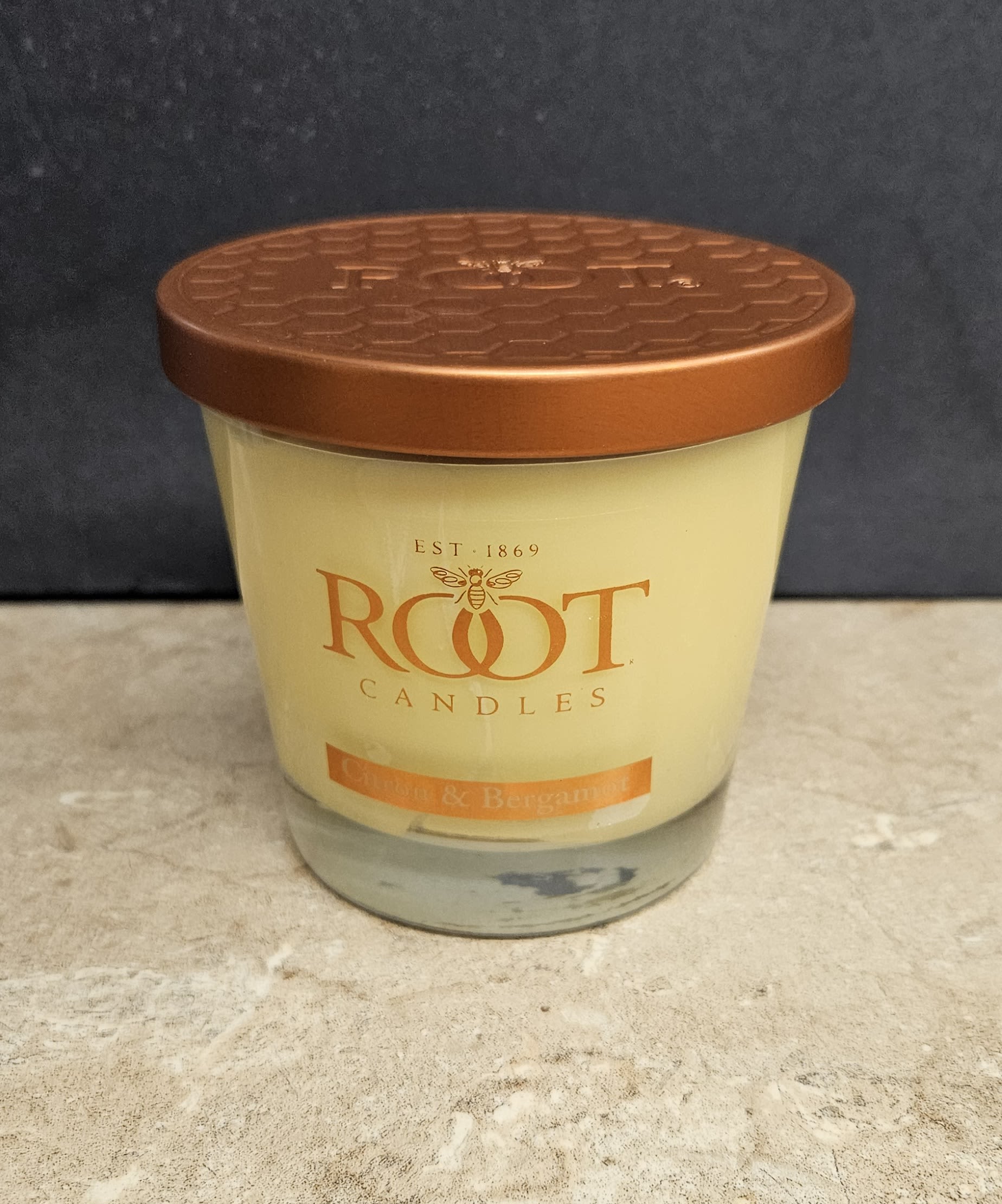Root Candle Tea Leaf &amp; Bergamot M - A warm, cozy housewarming gift that feels thoughtful the moment they set it down - this Root Candle tea leaf &amp; bergamot jar candle is ideal for a housewarming or everyday gifting. As a flower-arrangement shop pairing, think of it as the candle companion to an orange-and-white bouquet: the soft cream wax and rich orange label create an inviting focal point for entryway tables or bedside dressers, while the copper-colored metal lid and clear glass jar add a polished, modern touch.  The candle comes in a clear glass jar with cream-colored wax and a warm orange label, topped by a copper-tone metal lid that catches the light. The scent reads as currant &amp; bergamot, offering a bright, slightly fruity citrus aroma that's versatile for many rooms. Sized for easy gifting and display, this single jar candle pairs beautifully with autumnal or neutral floral arrangements and makes a reassuring, low-maintenance present that helps the person you're thinking of settle into their space.