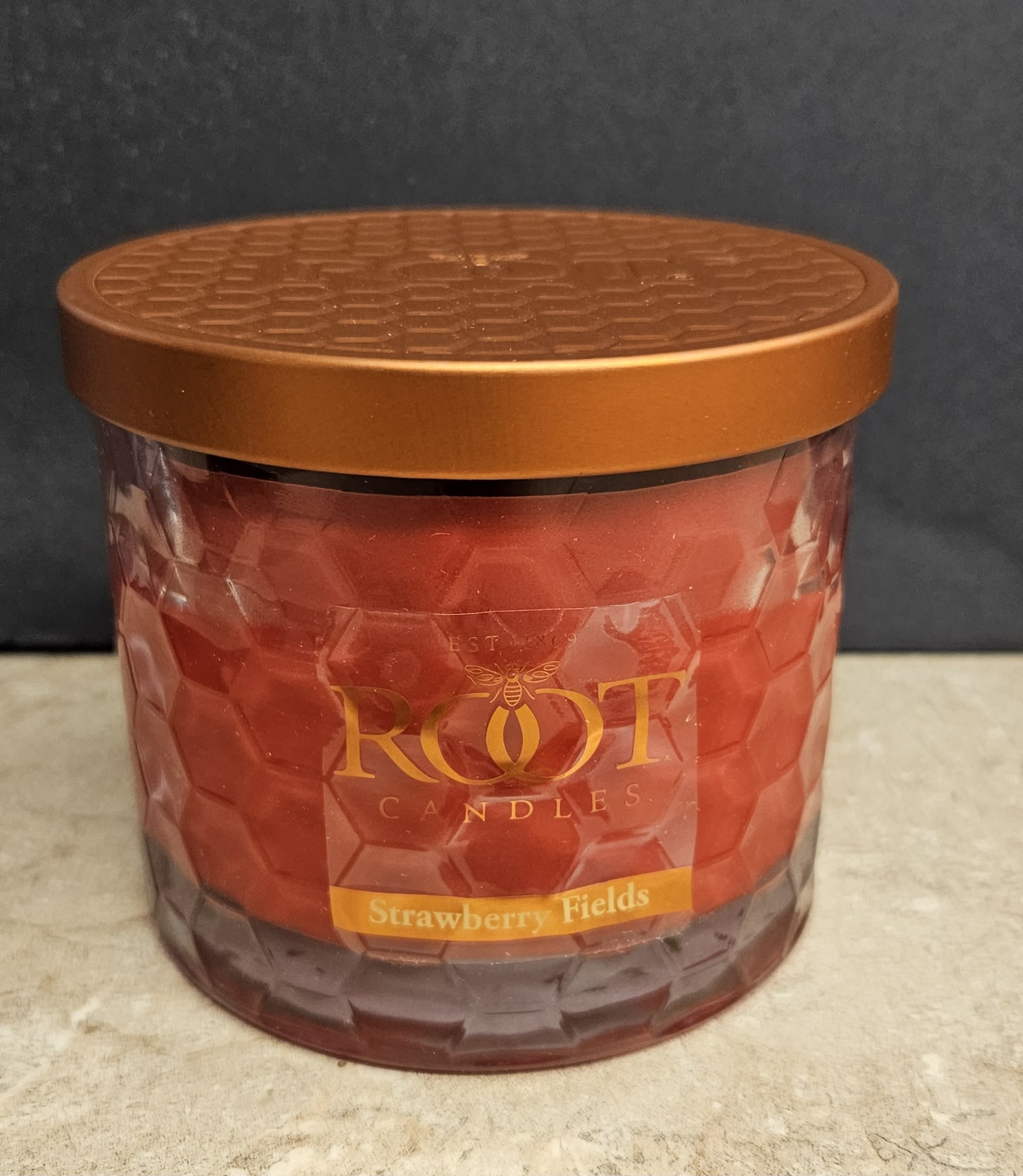 Root Candle Strawberry Fields 3 Wick - A richly hued strawberry-scented candle that makes a cozy gift for birthdays, hostess gifts, or to welcome someone home. This Root Candle Strawberry Fields L candle pairs deep red wax with a faceted glass jar and metallic gold lid for a warm, decorative look-perfect for adding fragrance and ambiance to living rooms, kitchens, or bedside tables.  The glass jar features a classic front label reading ROOT CANDLES with "Strawberry Fields" beneath, and the large size offers long-lasting scent throw. Colors are warm red with gold accents and a black label detail; the included metal lid helps keep fragrance fresh between uses. For care, trim the wick to 1/4" before each burn and allow the melt pool to reach the jar edge on first use to prevent tunneling-ideal as a thoughtful gift that fills the room with sweet, fruity fragrance.