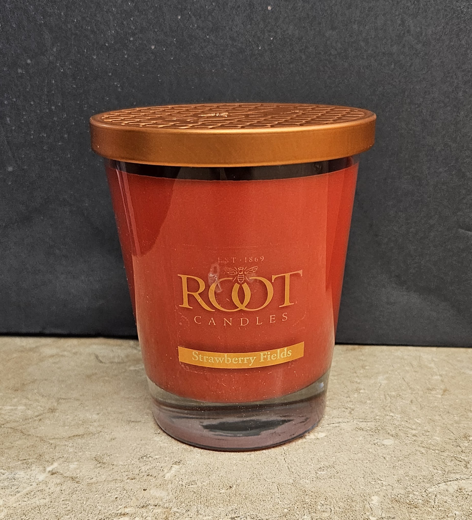 Root Candle Strawberry Fields L - A richly hued, fruit-forward home fragrance that reads like a cozy gift: this Root Candle Strawberry Fields candle brings the warmth and sweetness of ripe strawberries into any room. Perfect as a hostess gift, birthday treat, or a thoughtful "thinking of you" present, the scented candle pairs beautifully with floral arrangements or can stand alone to set a welcoming mood for a kitchen, living room, or bedside table.  The candle comes in a clear glass jar filled with deep red wax and topped with a gold-toned metal lid featuring a patterned top. A classic front label reads "ROOT CANDLES" and "Strawberry Fields," giving it an elegant, gift-ready look. Compact and decorative, it slips easily into gift sets or onto mantels and shelves; burn according to the included care instructions and trim the wick between uses for an even, long-lasting fragrance.