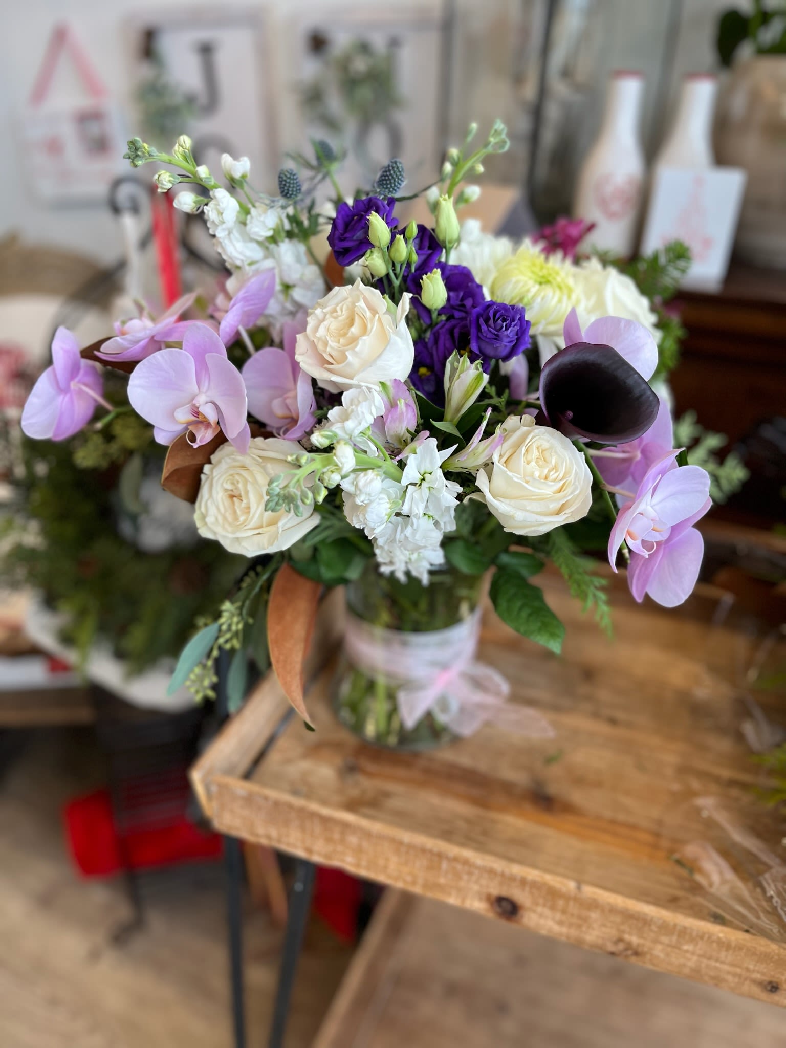 Mixed bouquet with orchids, roses, and purple blooms in a glass vase