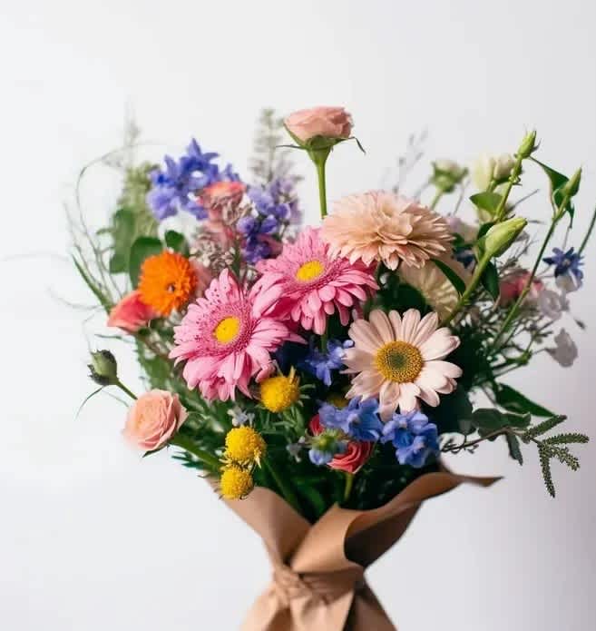 Mixed bouquet of pink, blue, and yellow flowers wrapped in brown paper