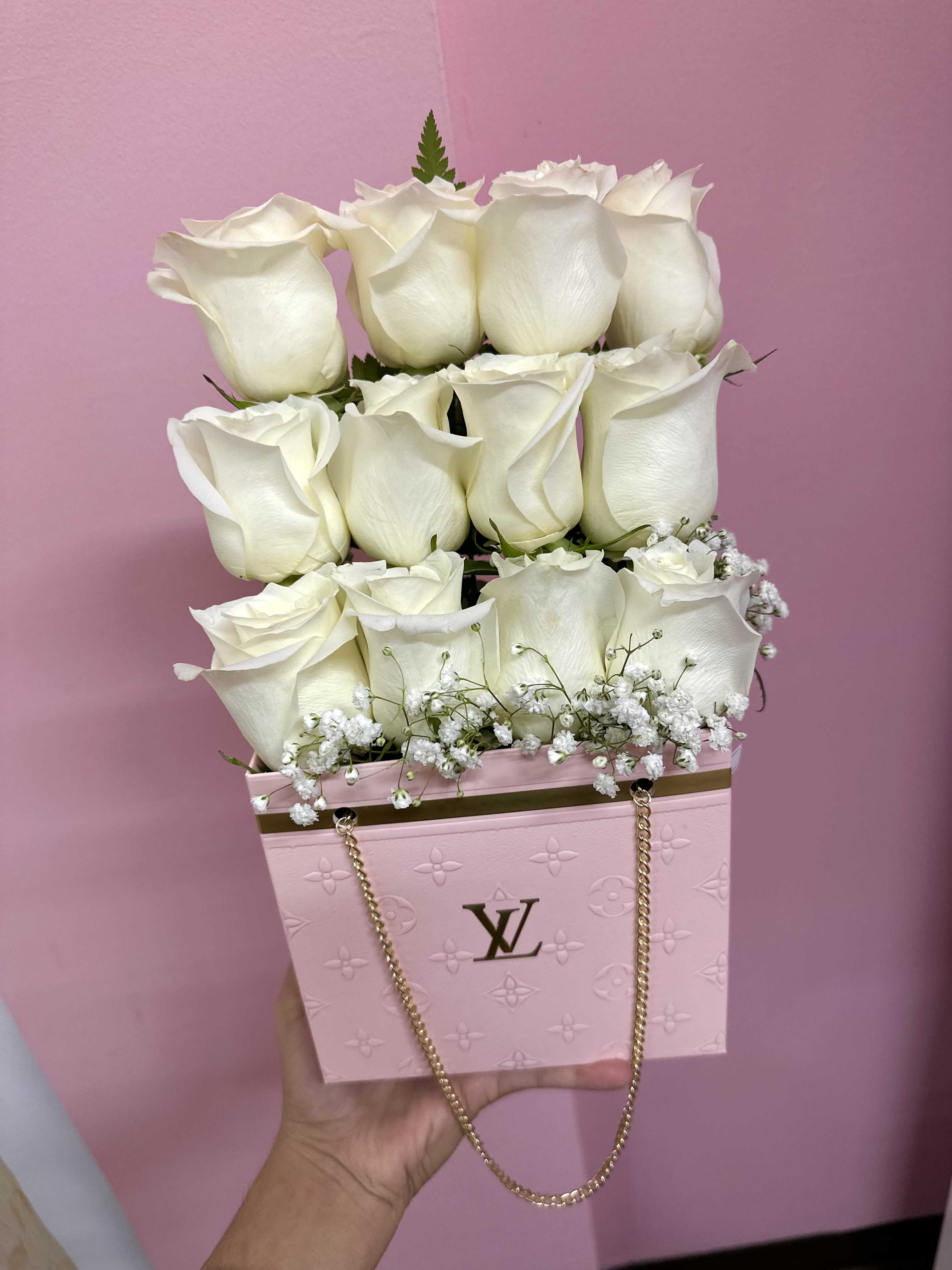 White roses arranged in a pink designer box with a gold chain handle