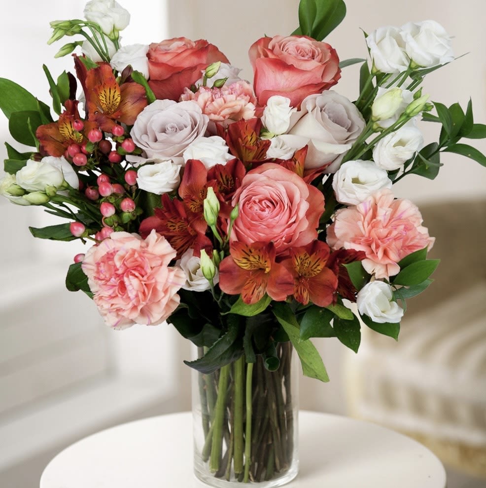 Mixed bouquet of pink, white, and orange flowers in a clear glass vase