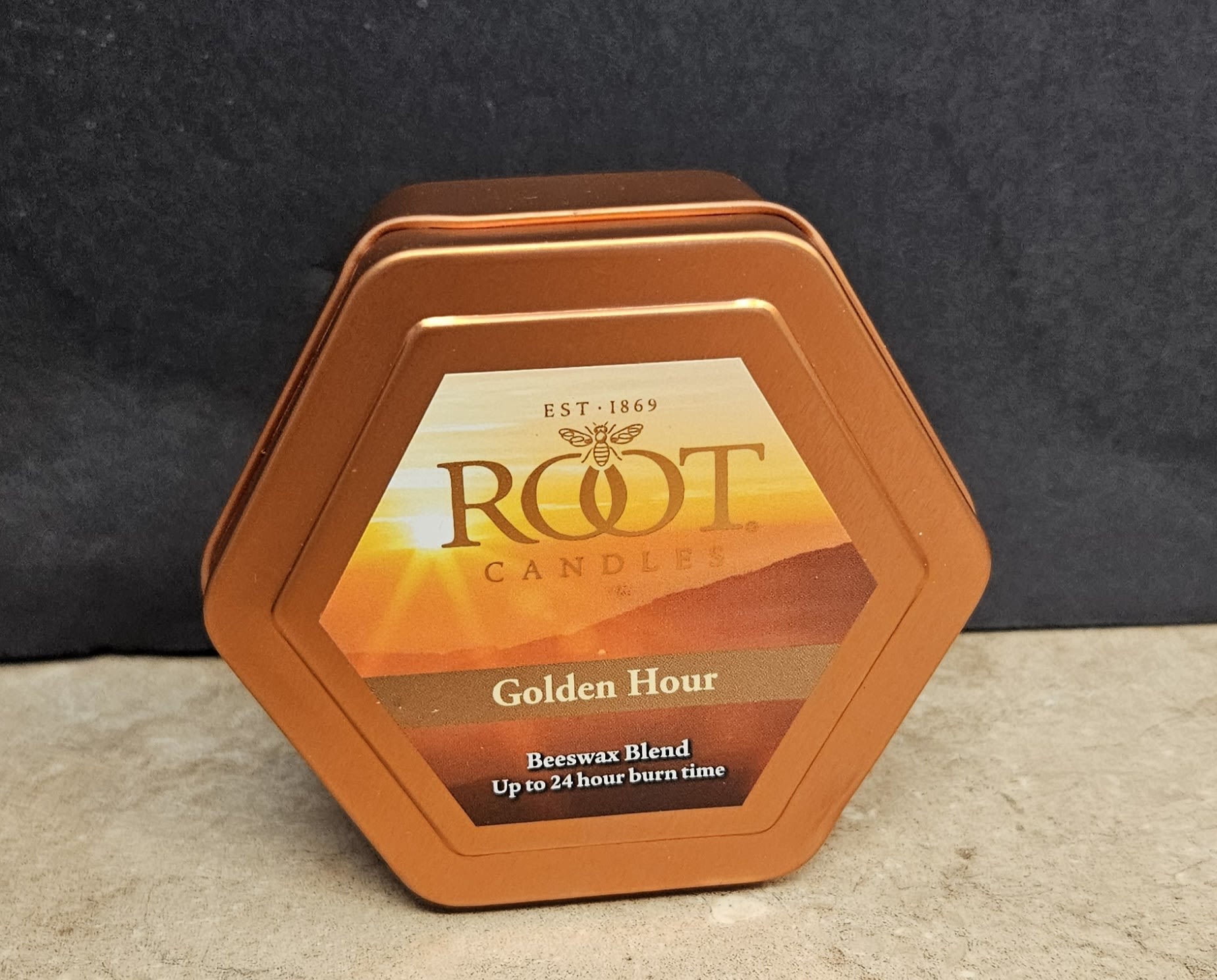 Root Candle Golden Hour Tin S - Warm, cozy autumn notes make this Golden Hour tin candle an ideal gift for someone who loves seasonal home fragrance - perfect as a birthday, housewarming, or Thanksgiving treat. The hexagonal metal tin in warm orange, with a sunset-gradient label in yellow, orange and brown, gives an immediate impression of late-afternoon warmth that will make the person you're thinking of feel comforted and noticed.  This Root Candle Golden Hour Tin S is a beeswax-blend candle presented in a sturdy metal container that's easy to place on a mantel, bedside table, or kitchen shelf. Colors on the tin are orange, yellow, black and white, and the label's sunset palette reinforces the cozy scent experience. With up to 24 hours of burn time, it's a simple, giftable option for seasonal décor or everyday fragrance - no extra wrapping required for a thoughtful, ready-to-give present.
