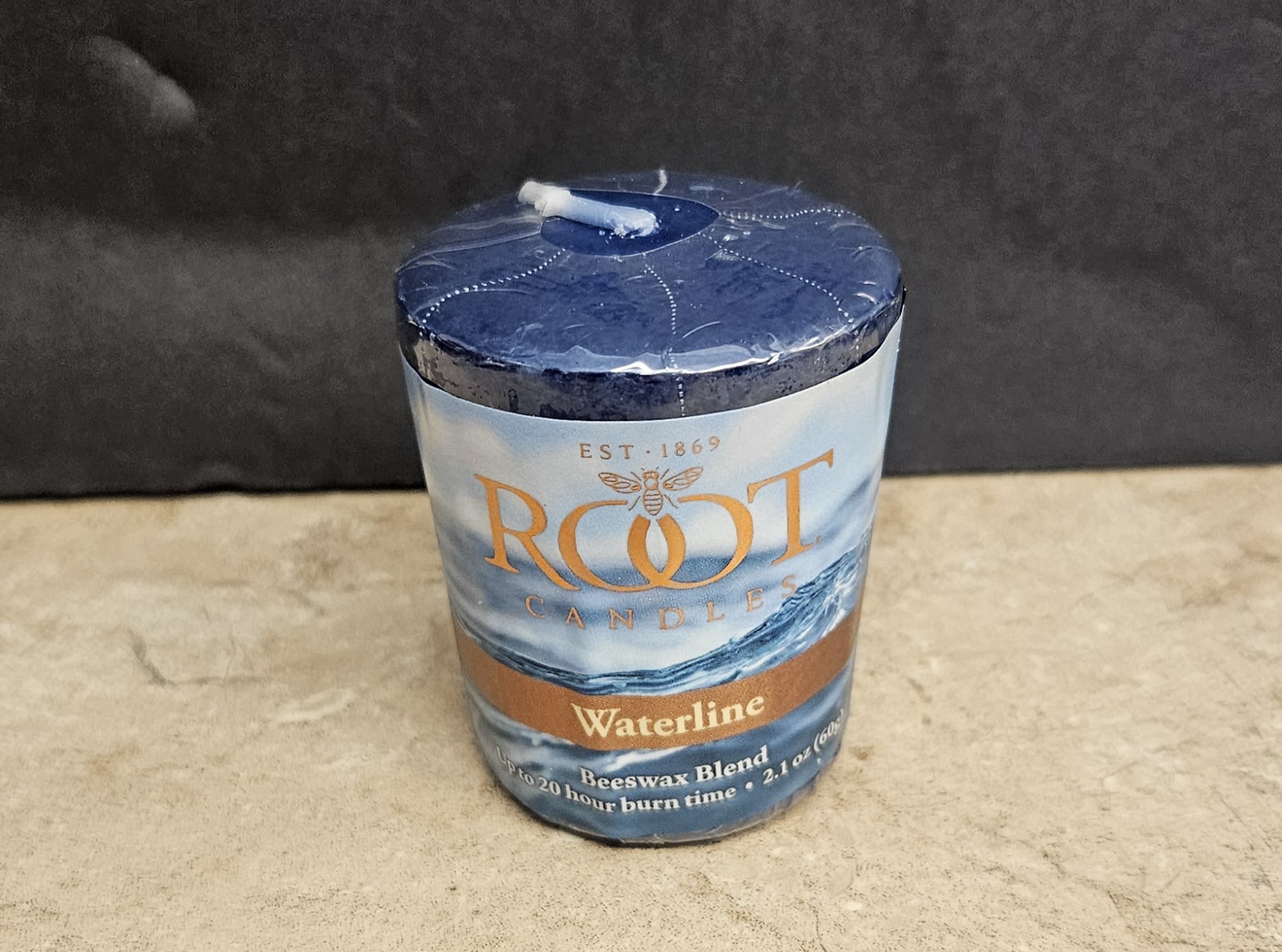 Root Candle Waterline S - A serene, ocean-inspired gift that brings a room together: this cylindrical Root Candle Waterline S is an ideal choice for housewarming or a thoughtful birthday present. As a candle gift for someone who loves coastal scents or calming decor, it complements blue-and-white floral bouquets and adds a warm, flickering focal point to living rooms, bathrooms, or bedside tables.  The candle comes sealed in clear plastic with a cool blue ocean-themed label and a deep navy top; accents of white and a touch of orange on the packaging give it a crisp, nautical look. Made from a beeswax blend, it arrives ready to display in its cylindrical container and pairs beautifully with blue hydrangeas, white lilies, or orange spray roses when assembled into an arrangement. Simple care: remove plastic before lighting and trim the wick to 1/4" between uses for a clean, even burn.  Whether you're creating a calming sympathy gesture, a coastal-themed anniversary surprise, or a cozy get-well gift, this candle makes the recipient feel cared for and seen. Its compact size works well as an add-on to bouquets or as a standalone present for someone who appreciates understated, fragrant home accents.