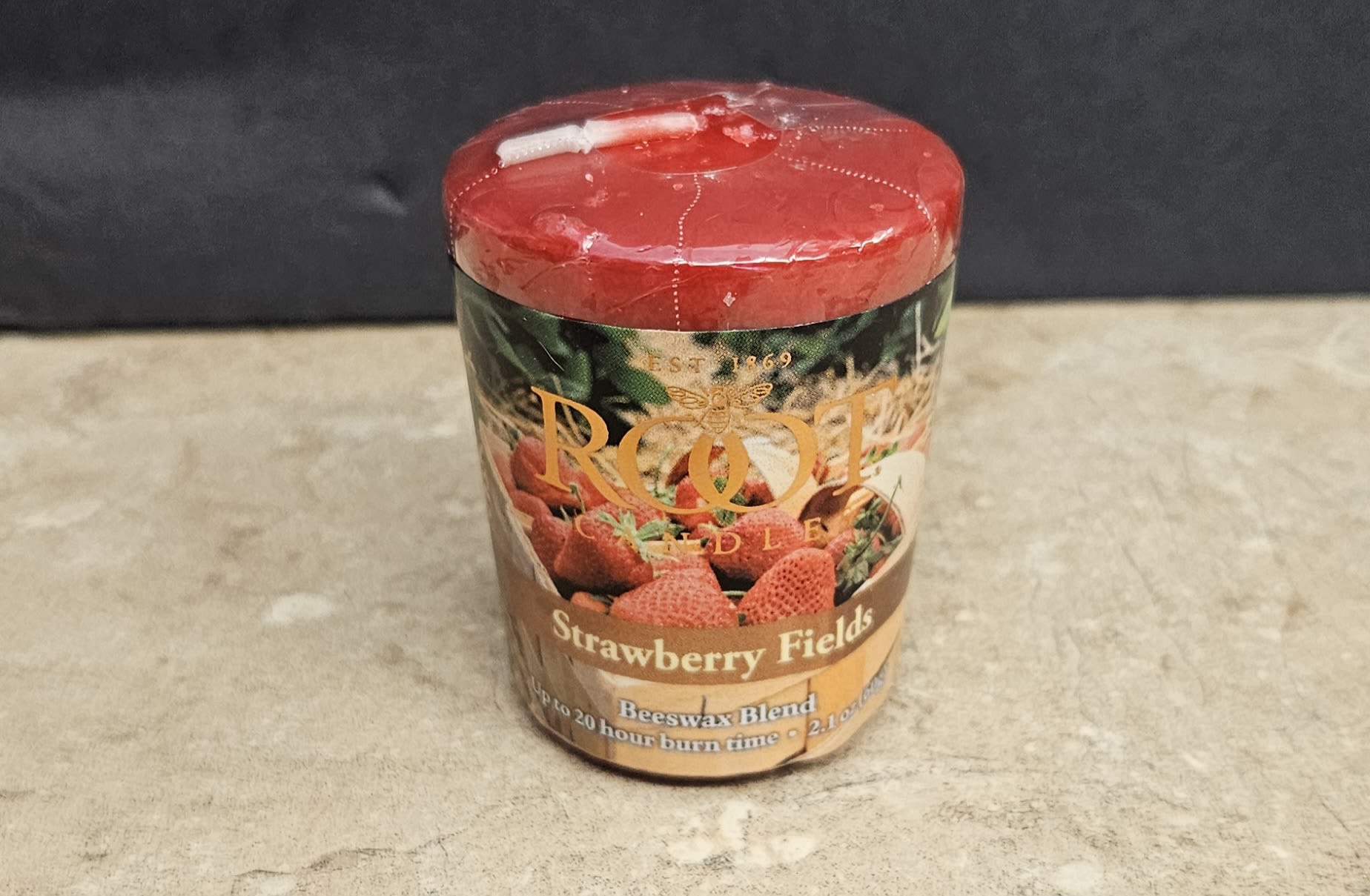 Root Candle Strawberry Fields Votive - A cozy, giftable votive that celebrates sweet summer nostalgia-this Root Candle Strawberry Fields votive makes a charming add-on gift or stocking stuffer for birthdays, housewarmings, or seasonal treats. The small flower arrangement category listing highlights it as a complementary item for customers buying bouquets or gift sets, and the Strawberry Fields scent and red-topped jar pair naturally with romantic or casual occasions like Valentine's Day, anniversaries, or a cheerful "just because" surprise.  The compact cylindrical jar features a warm red lid, a printed label with strawberries and "Strawberry Fields," and a tan-and-red palette that reads rustic and homey rather than floral. Sized for bedside tables or kitchen counters, it arrives ready to gift with a simple lid and branded label-perfect for someone who loves sweet, cozy fragrances and a touch of vintage charm.
