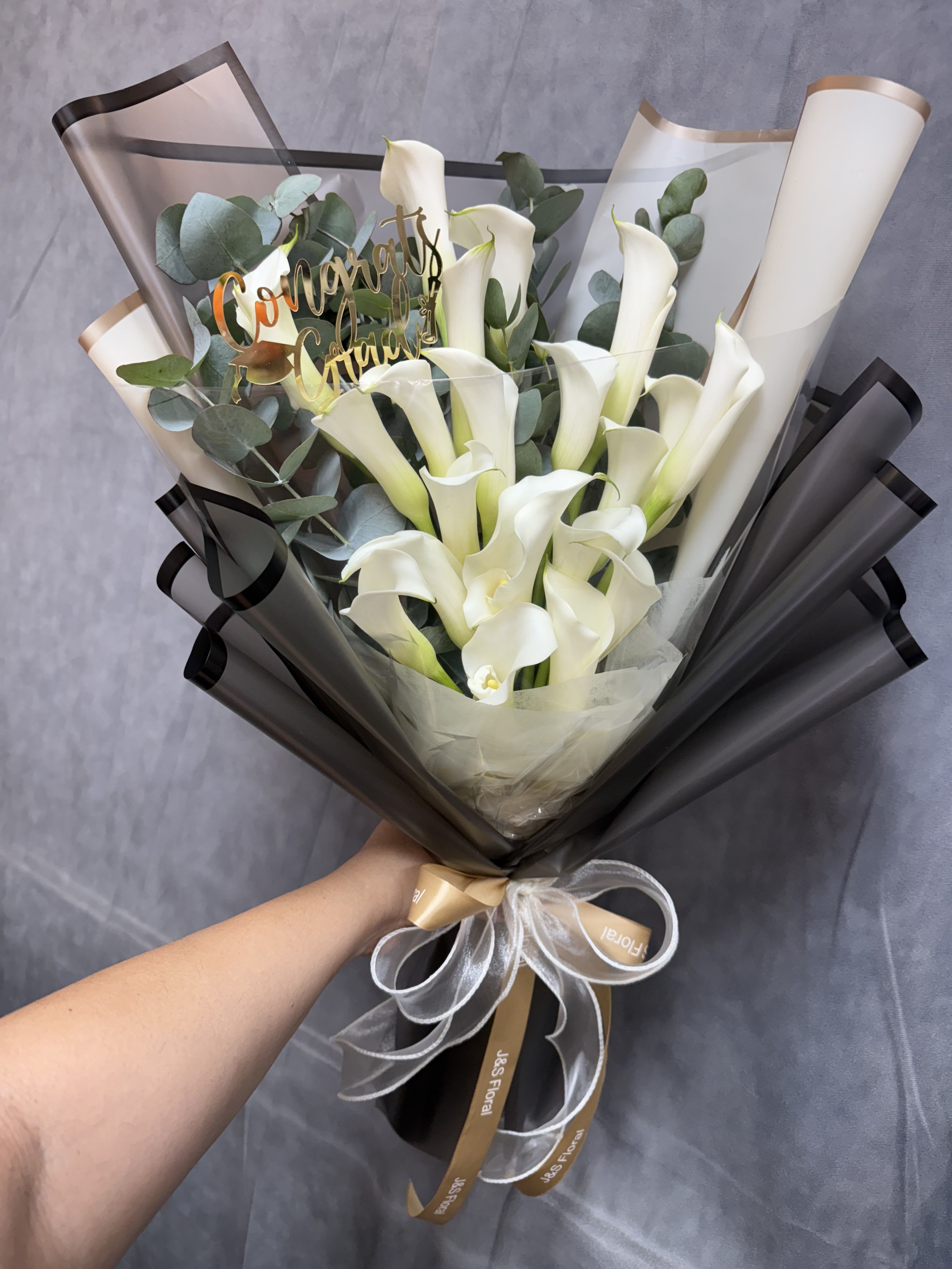Calla lilies lovers bouquet - White calla lilies with eucalyptus, wrapped in black and translucent paper with ribbon and a gold congratulatory pick-elegant, modern bouquet for graduations, birthdays, anniversaries, sympathy, or just because.   The congratulations stick can be changed to match your occasion 