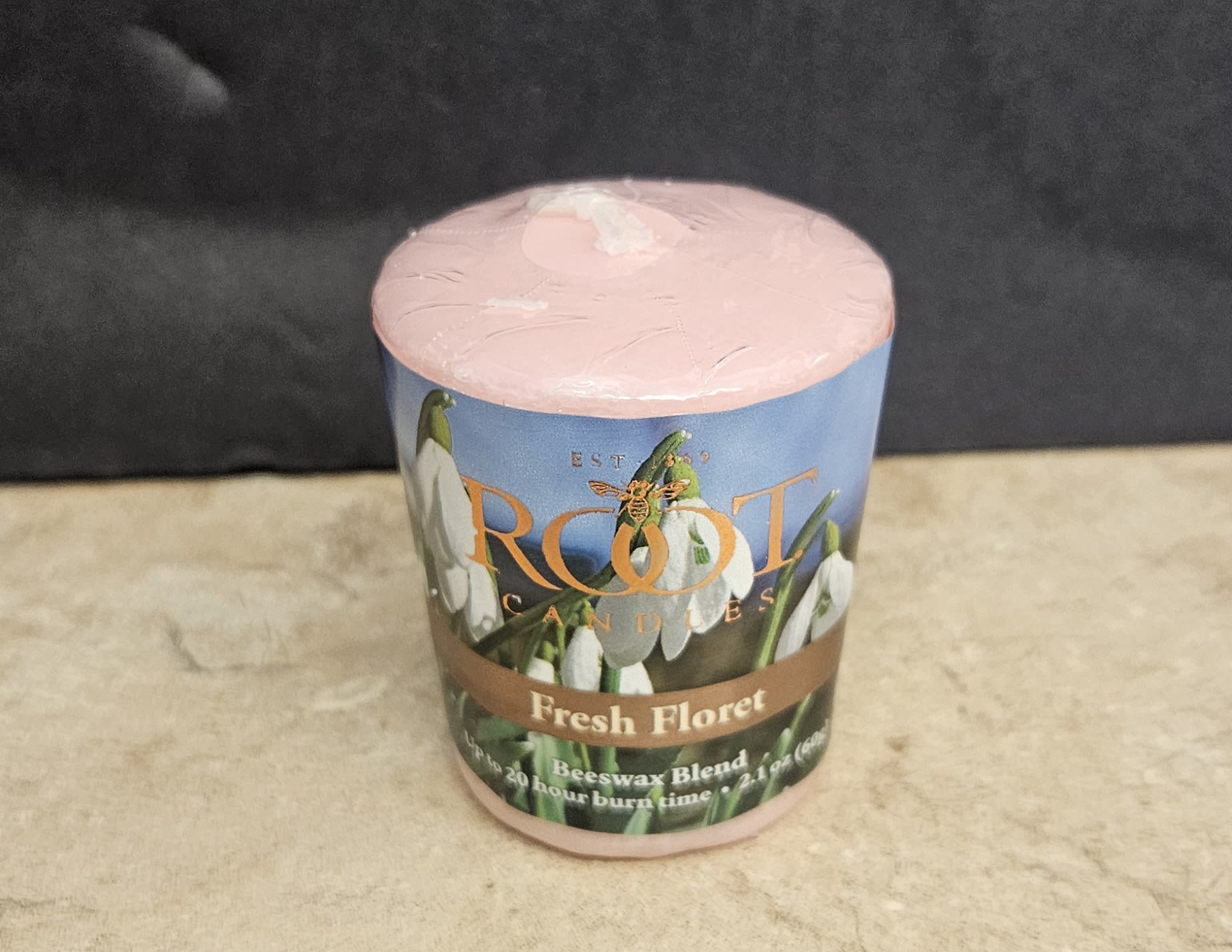 Root Candle Fresh Floret Votive - A softly botanical gift that reads like spring in a jar, this flower arrangement pairs a single pink votive candle with a printed floral container labeled "Fresh Floret" - perfect as a thoughtful gift or small housewarming present. Designed for someone who appreciates subtle, nature-inspired accents, this votive works well for birthdays, thank-yous, or as a sweet "thinking of you" token that brightens a bedside table or bathroom shelf.  The pink cylindrical candle sits in a printed container featuring delicate white, snowdrop-like blooms and the words "Beeswax Blend," giving the piece a clean, fresh aesthetic. Accented visually by hints of blue, white, and soft orange tones on the label, it feels like a mini floral arrangement even though it's a scented home accessory. Ideal for gifting on its own or paired with a small bouquet, the votive is compact and ready to present - a simple way to make the person you're thinking of feel seen and comforted.