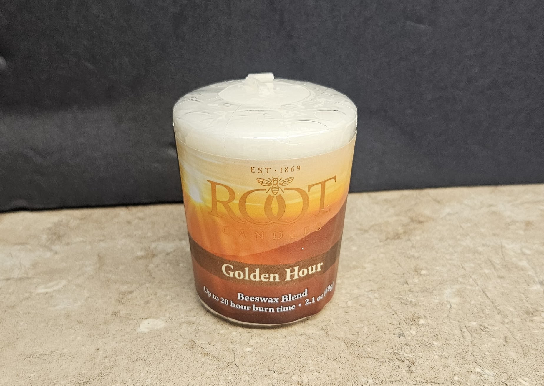 Root Candle Golden Hour Votive - The warm amber glow of the Golden Hour votive instantly suggests cozy evenings and thoughtful gifting - a home fragrance votive perfect for housewarmings, hostess gifts, or a simple way to say you're thinking of someone. This candle votive and its autumnal label pair the product type (flower shop gift, home fragrance) with occasions like seasonal décor, thank-you gifts, and everyday comfort.  Poured beeswax with a pale, creamy surface sits in a clear glass jar topped with a matching lid; the printed label reads Root Candles and Golden Hour / Tea Leaf &amp; Honey, giving a subtle honeyed, tea-inspired impression. Colors range from soft white wax to warm amber-brown label tones with black printed text, creating a clean, understated look that complements rustic or modern interiors. The compact cylindrical size makes it easy to place on a mantel, bedside table, or kitchen shelf.  Choose this votive when you want the person you're gifting to feel soothed and well cared for - the kind of small luxury that makes a home feel intentional. It arrives ready to display; burn on a heat-safe surface and trim the wick as recommended for the longest, cleanest burn.