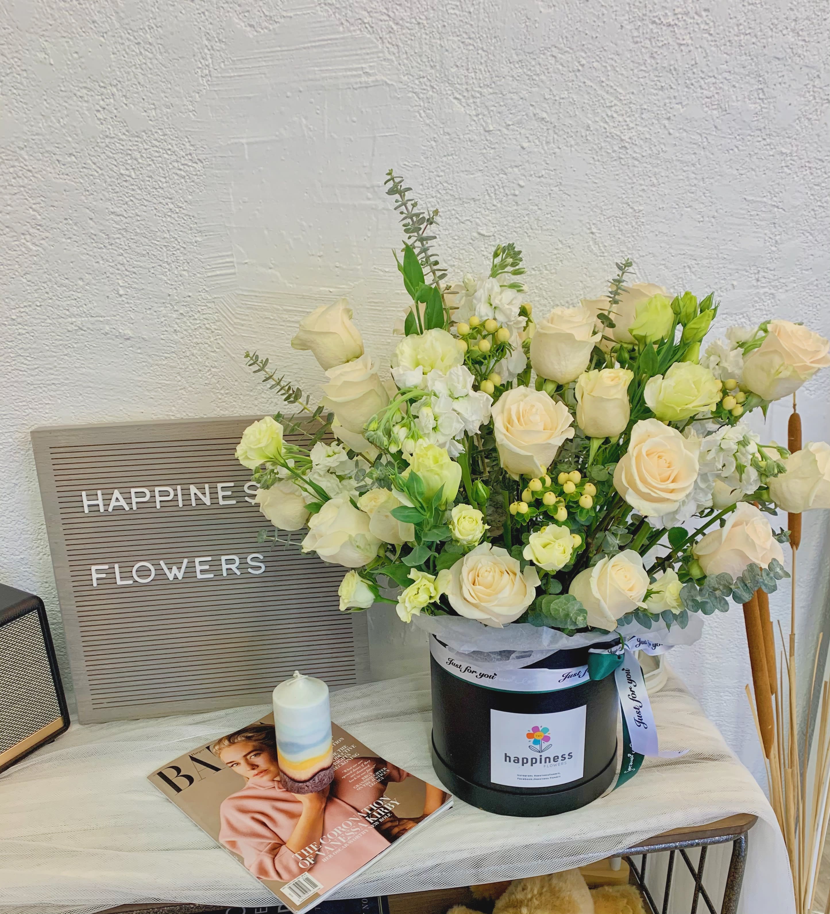Cream roses and white blooms arranged in a black hat box with a ribbon.