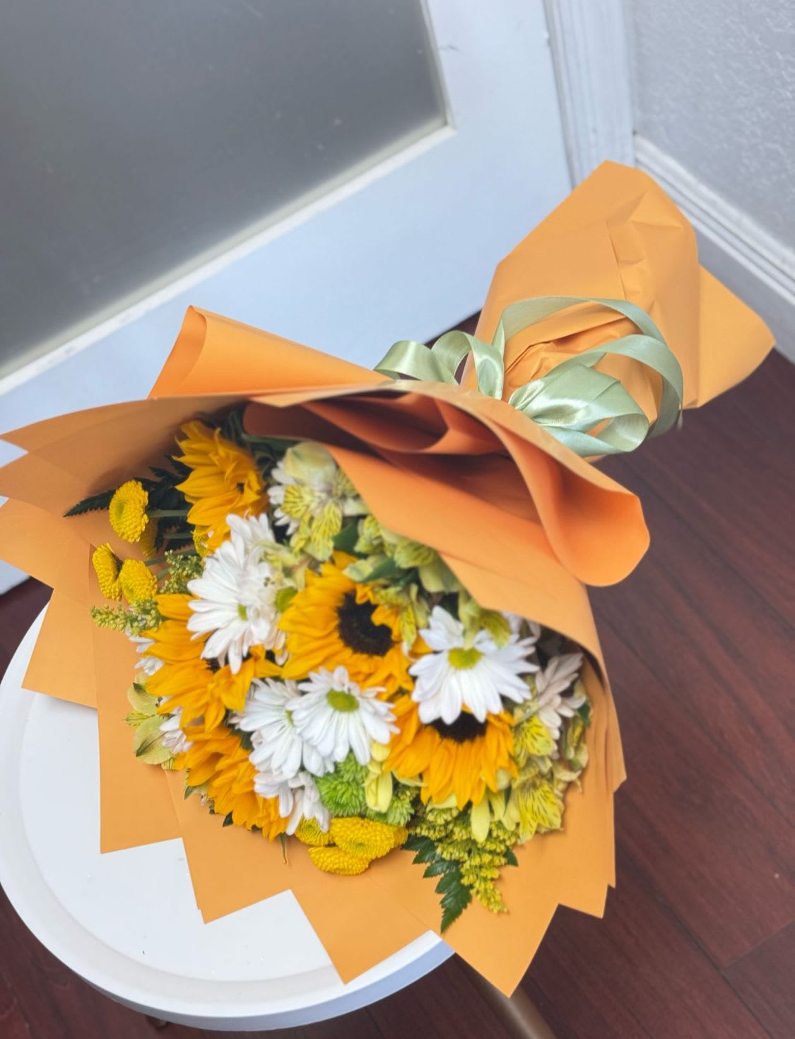 Bouquet of yellow sunflowers and white daisies wrapped in orange paper