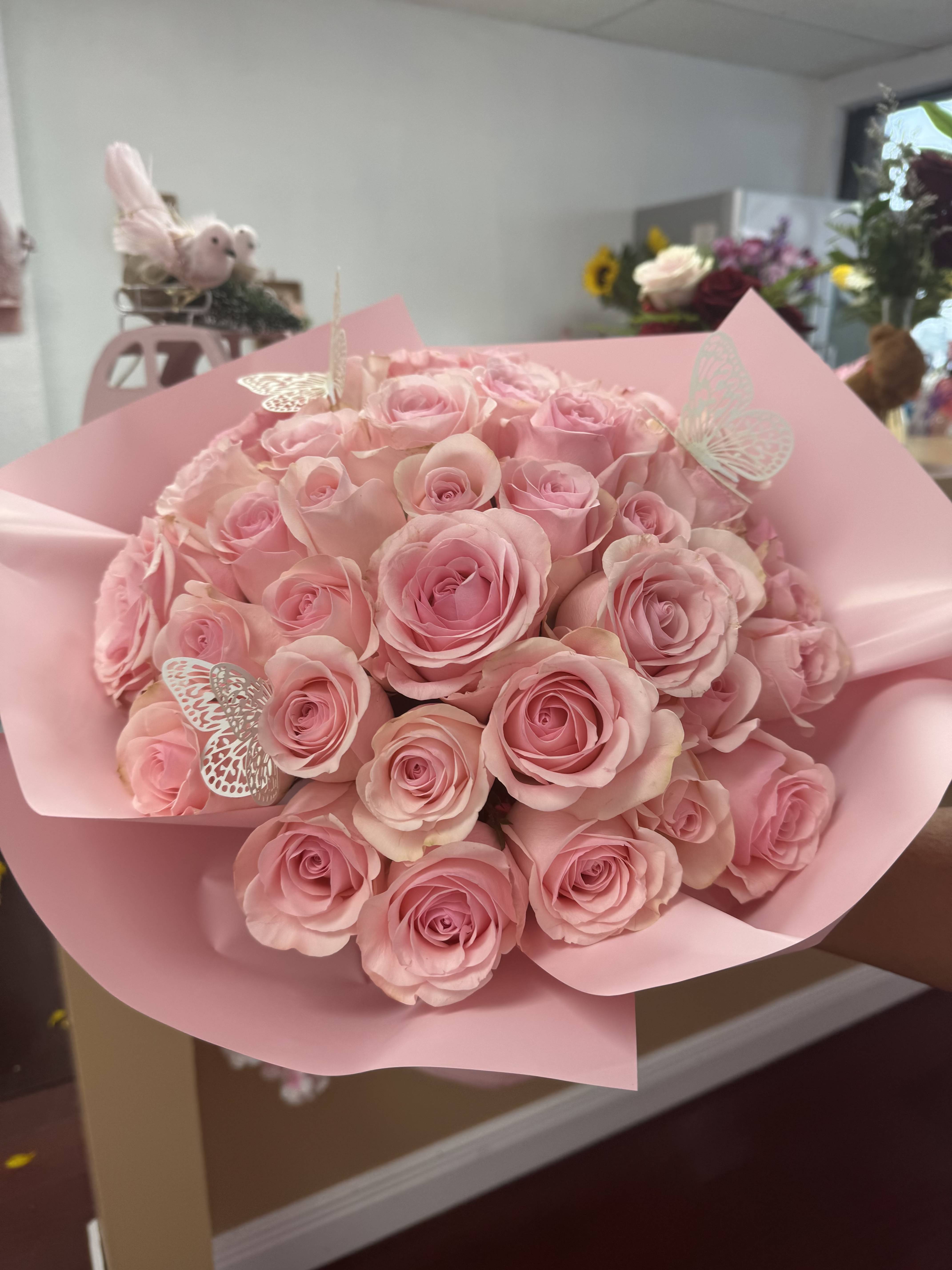 Bouquet of pink roses wrapped in pink paper with butterfly picks