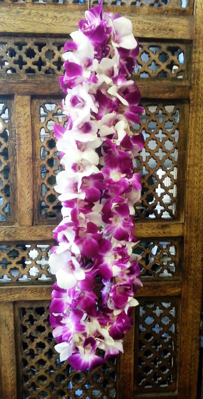 Purple and white orchid lei draped over a carved wooden panel
