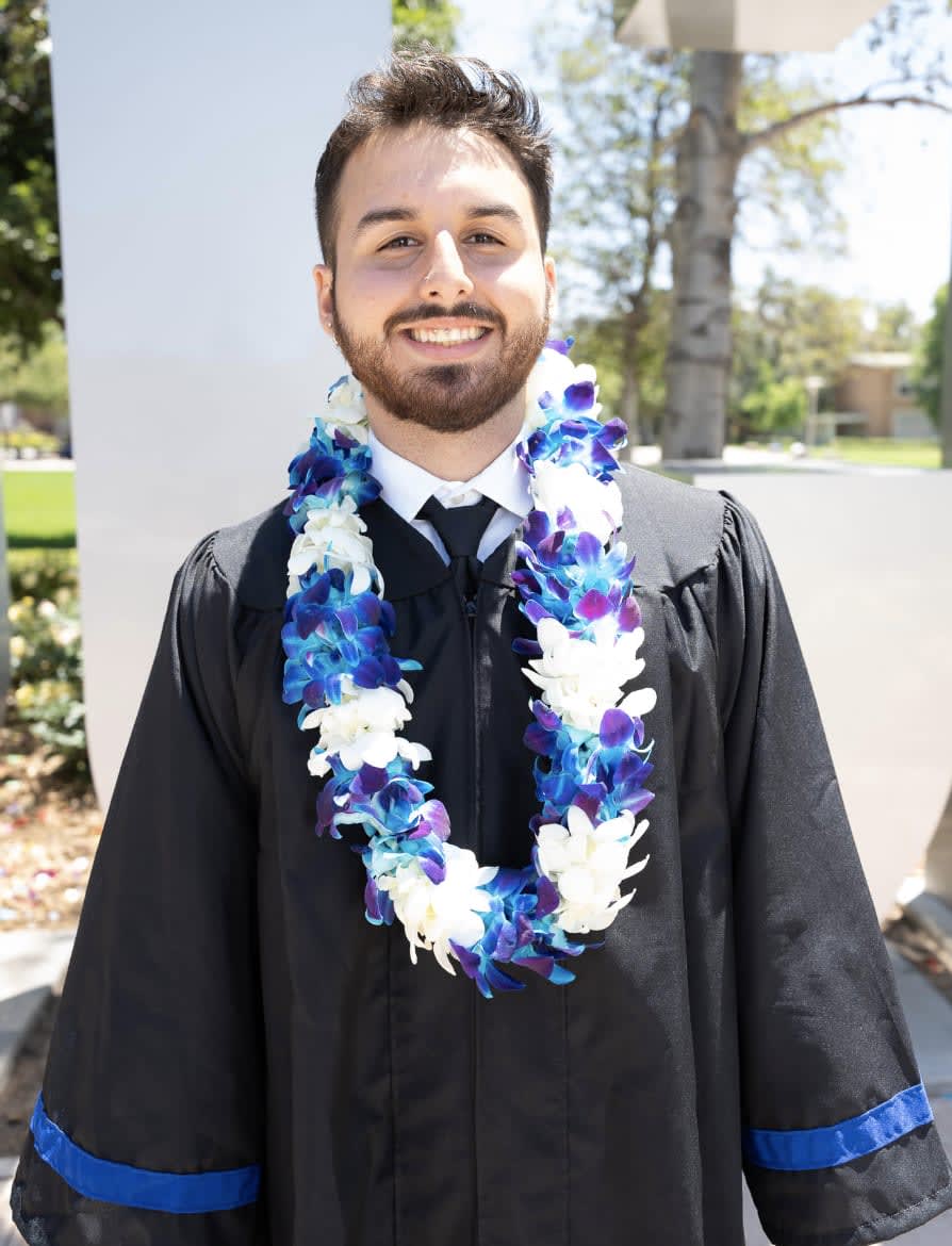 Man in graduation gown wearing a blue and white flower lei