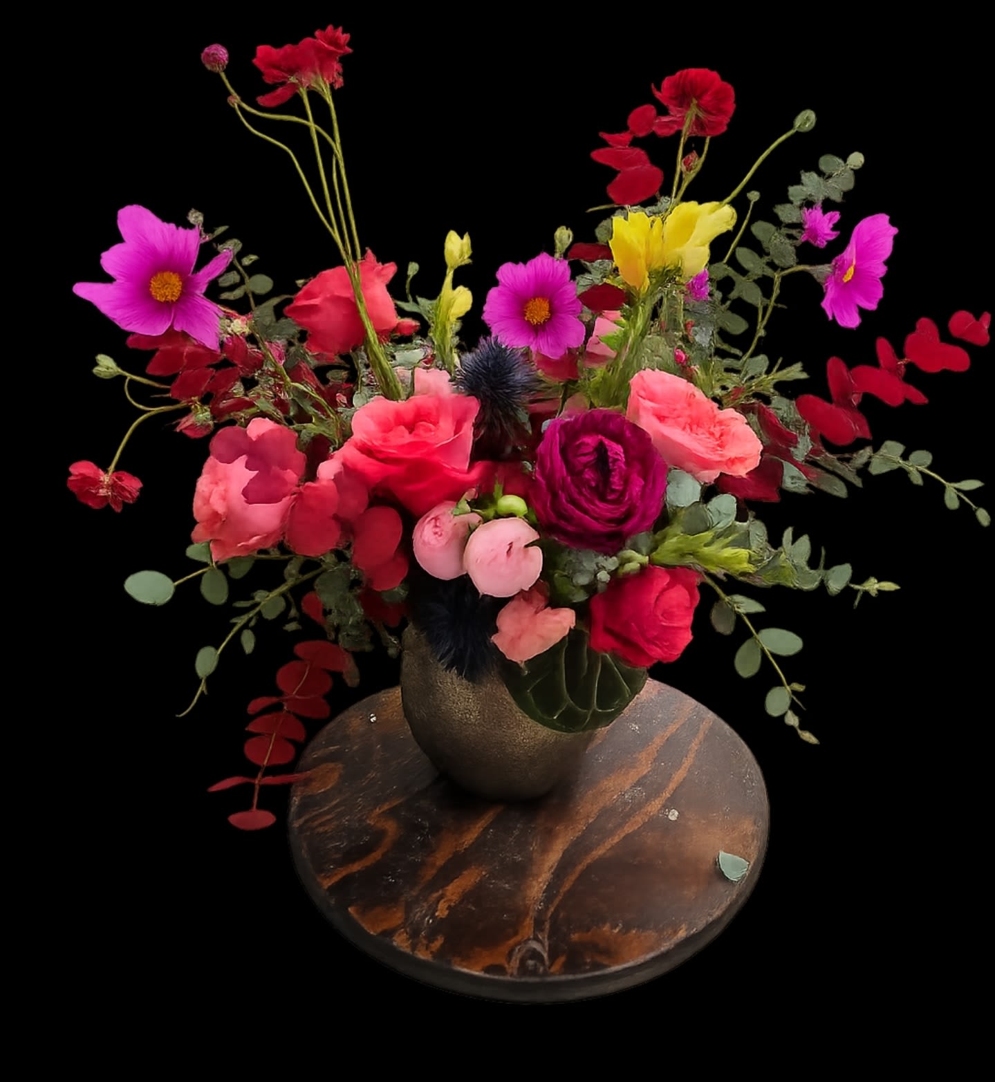 Artsee - Bold, garden-fresh color greets the recipient with this lively flower arrangement-perfect as a birthday bouquet, anniversary surprise, or a bright thank-you gesture. Loose, airy stems in vivid pinks, reds, yellows, purples, and mixed tones create a playful yet romantic statement that makes the person you're thinking of feel celebrated and genuinely seen.  A mix of anemones, ranunculus, roses, daisies, carnations and other seasonal blooms are gathered in a dark ceramic vase set on a round wooden base. Layered, round blossoms contrast with daisy-like faces and ruffled petals while eucalyptus-style foliage and trailing stems add natural movement and an asymmetrical, garden-inspired silhouette. The arrangement's size and fullness read as generous without being formal, bringing a contemporary, hand-picked look to any room.  Ideal for everyday gifting or marking special moments, this arrangement arrives ready to display in its ceramic vessel on the included wooden base. To keep blooms looking fresh, replace vase water every 2-3 days and trim stems at an angle if you transfer them-small care steps that help the bouquet stay vibrant through the week.