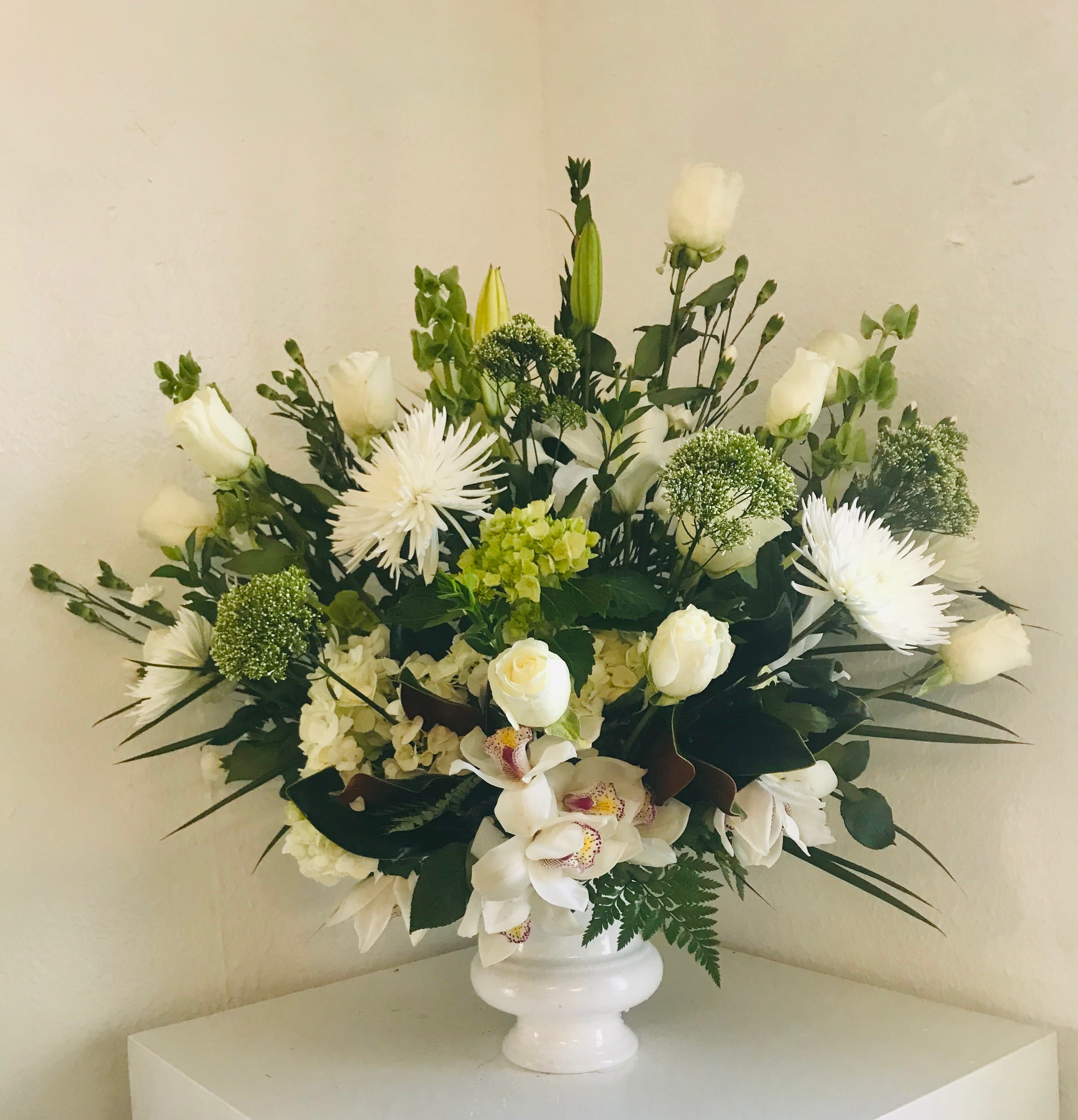 White floral arrangement in a white vase with roses and orchids